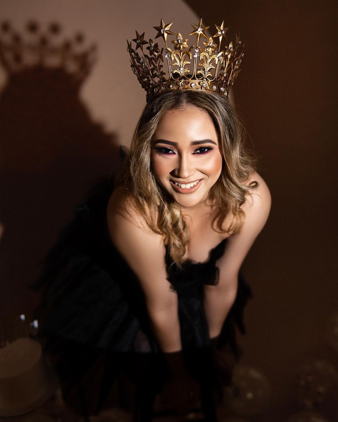 Dramatic portrait featuring ornate gold crown against brown backdrop.
