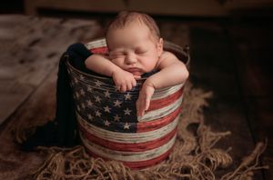 Newborn baby boy in an American flag bucket on a wood floor in McKinney, Texas.