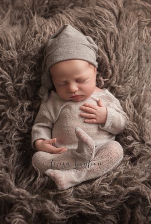 Newborn baby boy wearing a gray romper and sleepy hat laying on a wool rug in Allen, TX.