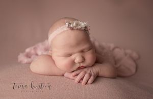 Newborn baby girl laying on a pink blanket wearing a pink flower headband in DFW, Texas.
