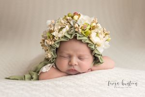 Newborn baby girl laying on a cream blanket wearing a flower bonnet in Frisco, TX.