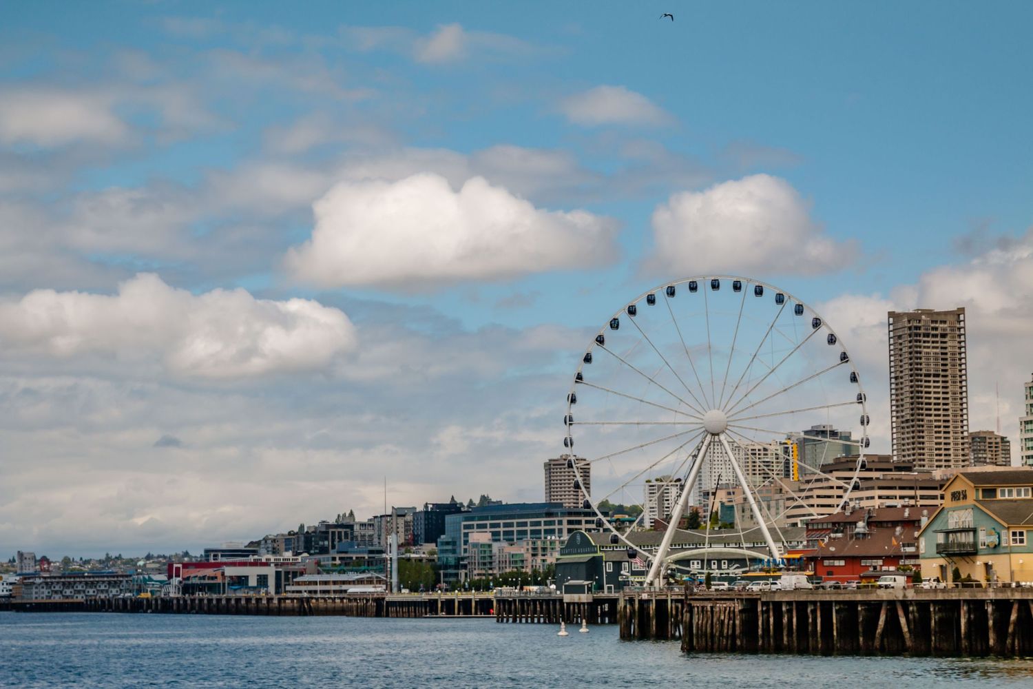 The Seattle skyline with blue sky, and white puffy clouds, with the Ferris wheel along the waterfront.
