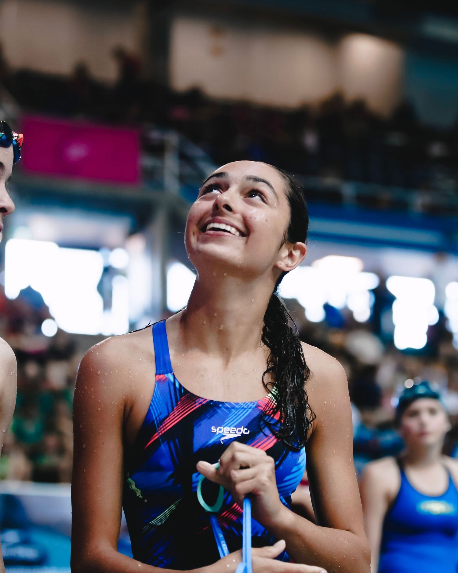 Swimmer in blue swimsuit smiling at indoor pool competition.