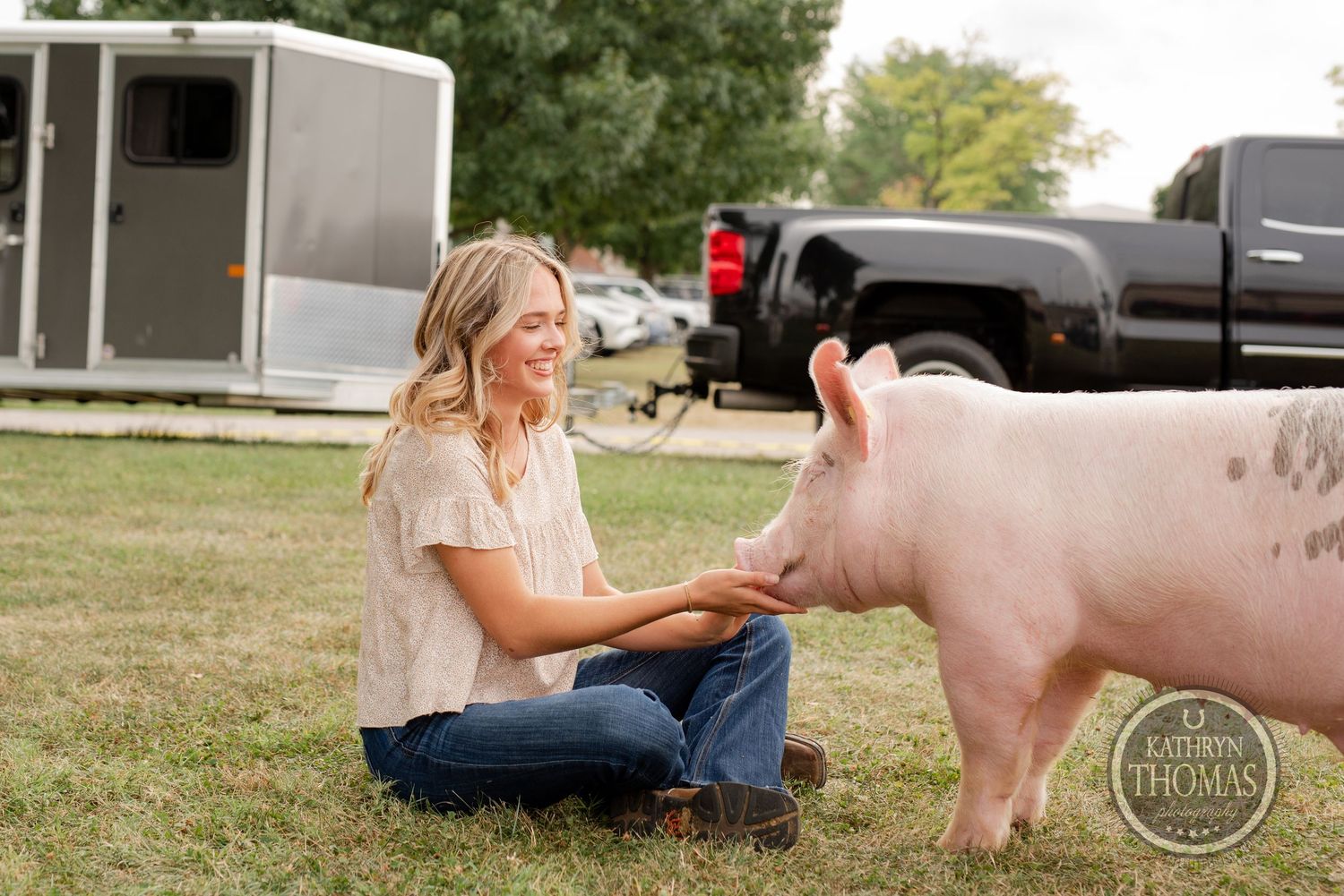 A pink pig sits in the grass next to someone wearing jeans and a light colored shirt.