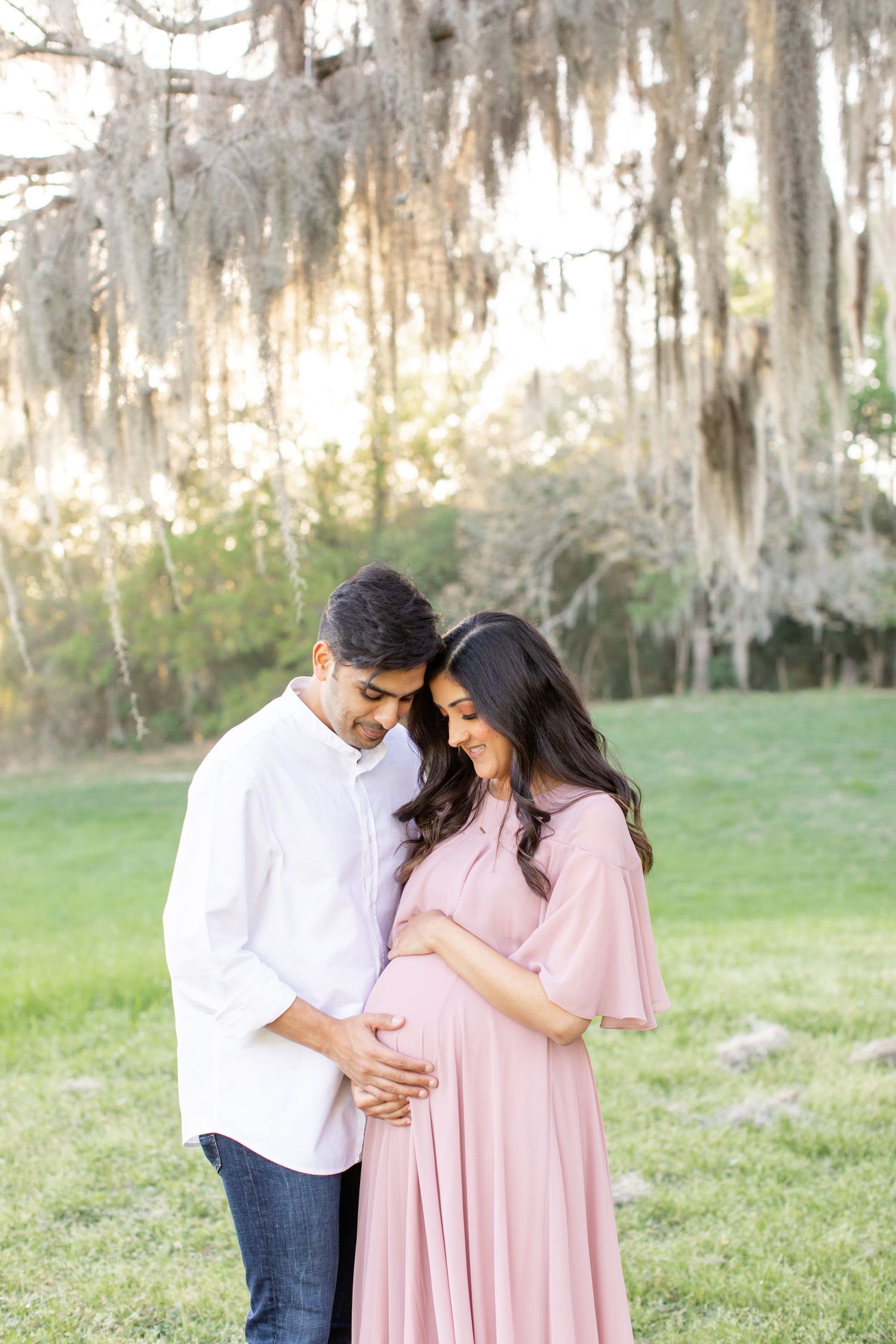 Expecting parents share tender moment while cradling baby bump in outdoor setting.