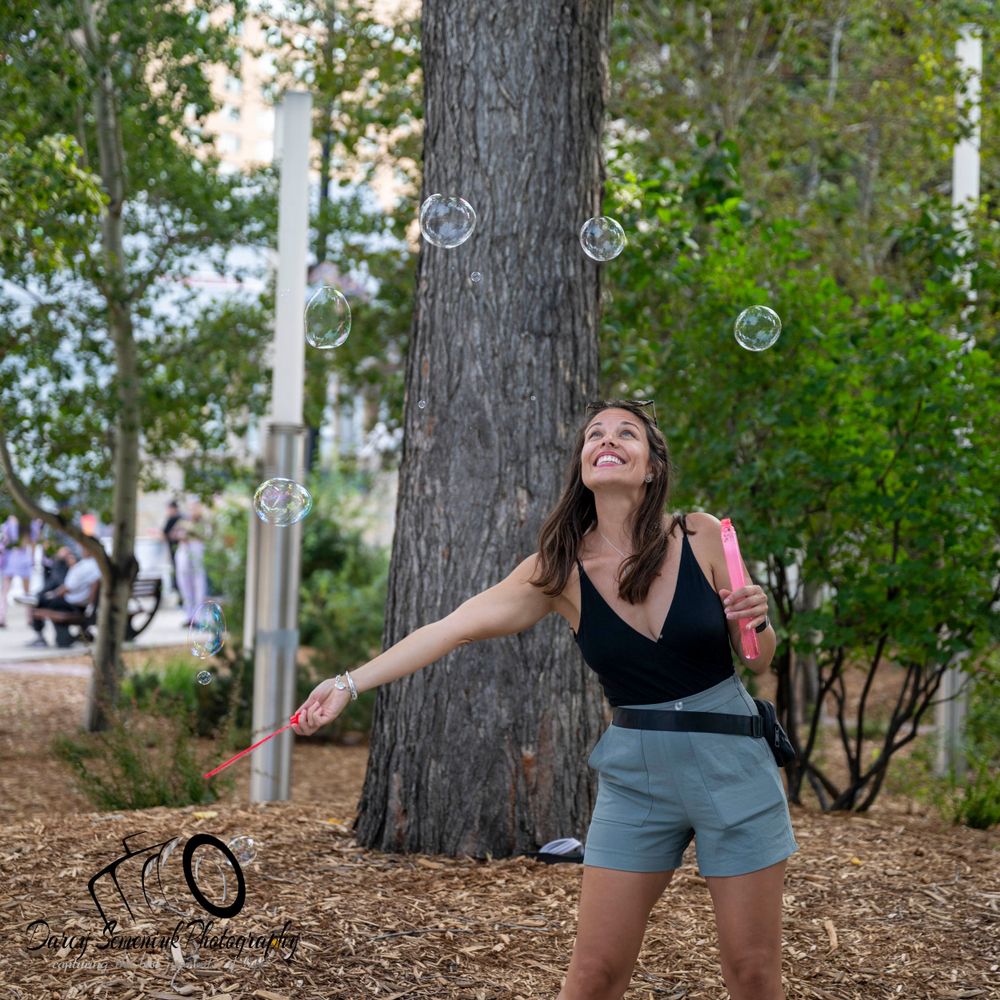 Person playing with soap bubbles in a wooded outdoor setting during a sunny day.