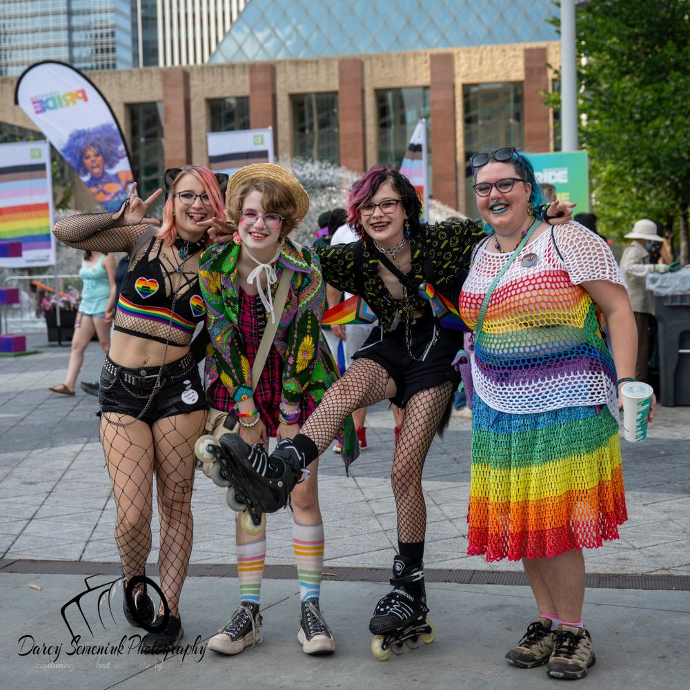 Group of people in colorful outfits and roller skates posing together at a Pride festival celebration outdoors.