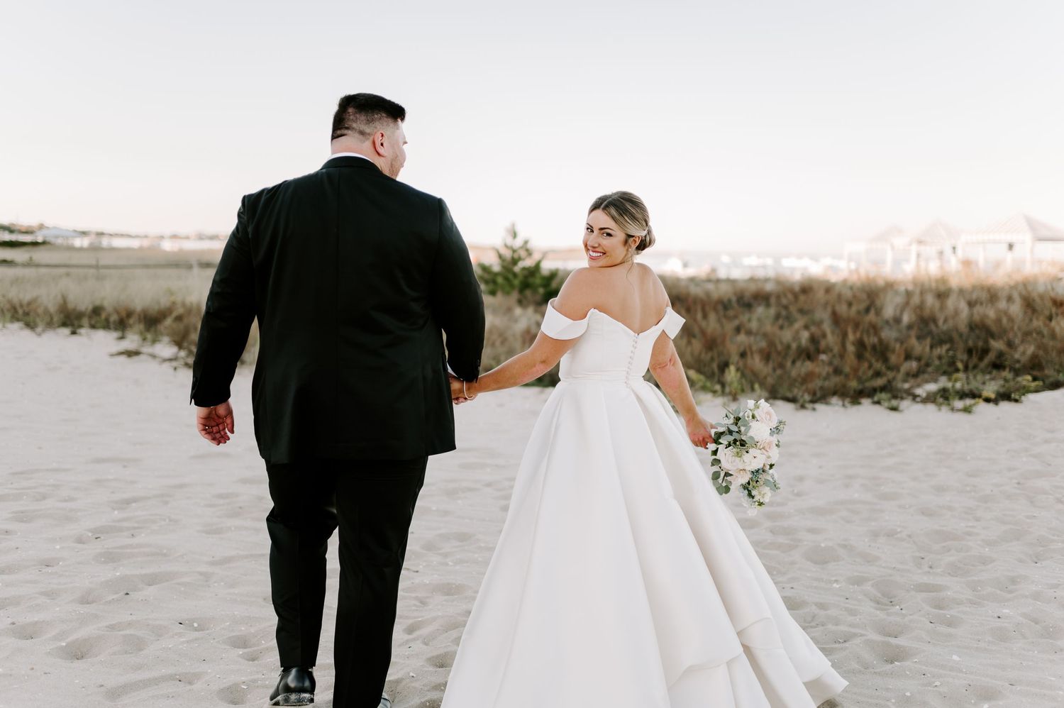Elegant couple walks along pristine beach at sunset in formal attire.