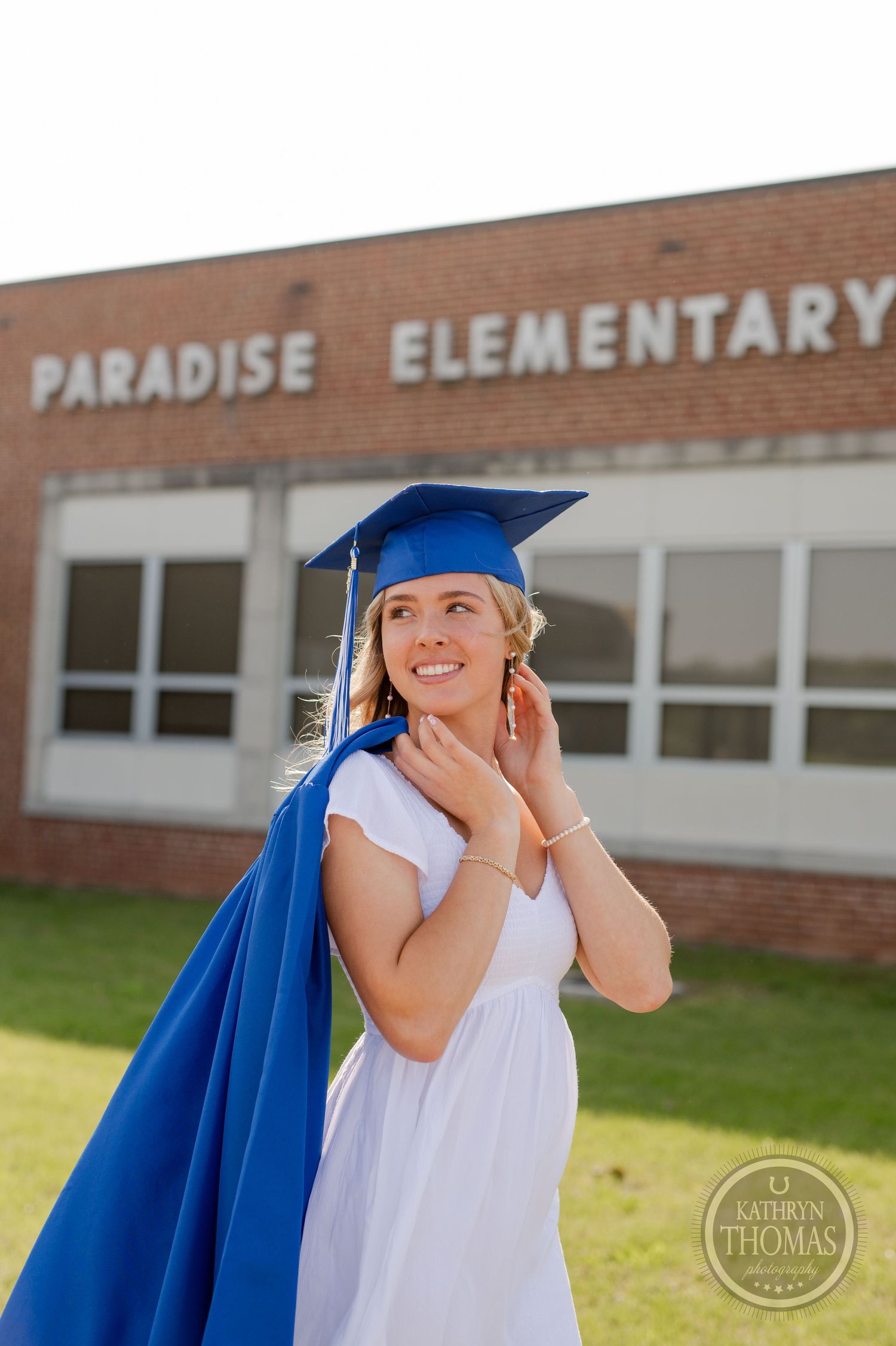 Graduate in blue cap and white dress poses cheerfully at Paradise Elementary school.