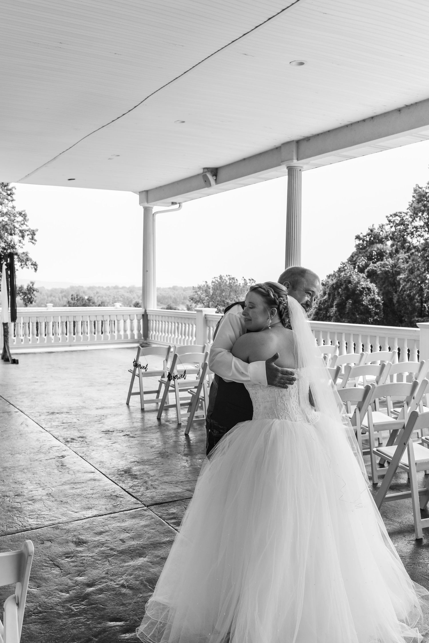 A black and white wedding moment captured on a covered porch with chairs set up for ceremony.