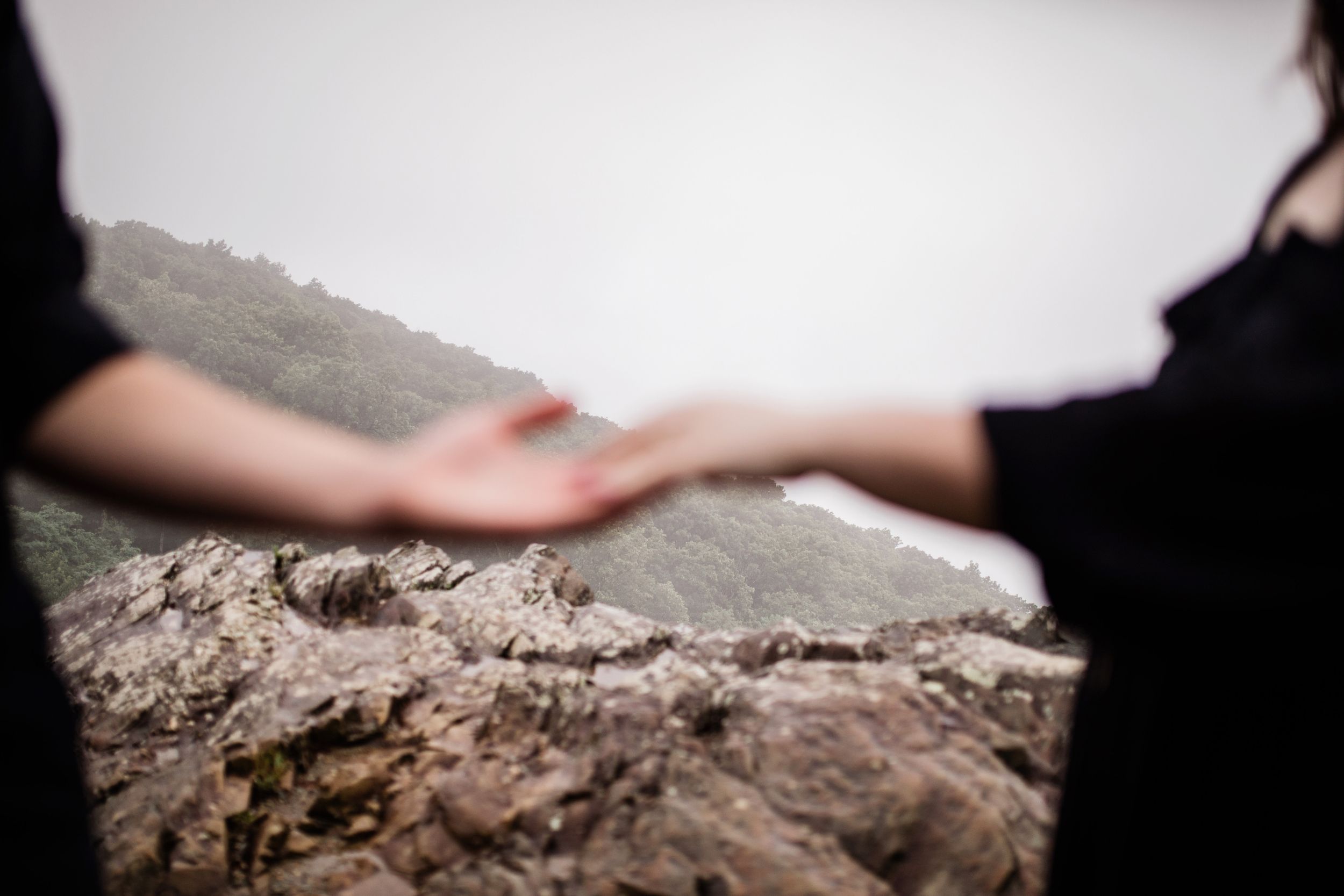 Blurred couple reaching toward each other on rocky mountain overlook with misty valley below.