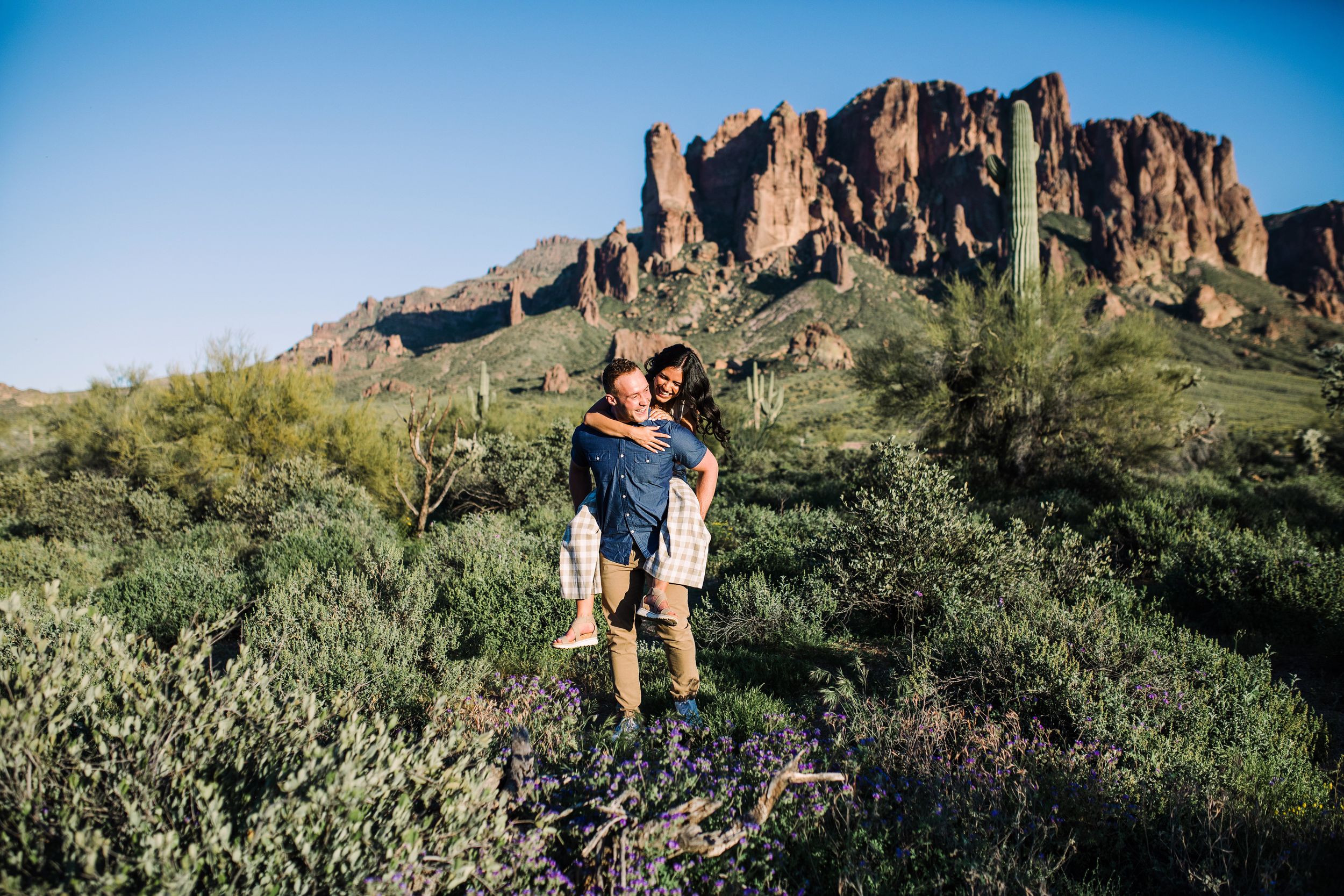 Couple enjoying a piggyback ride with stunning red rock mountain backdrop in Arizona.