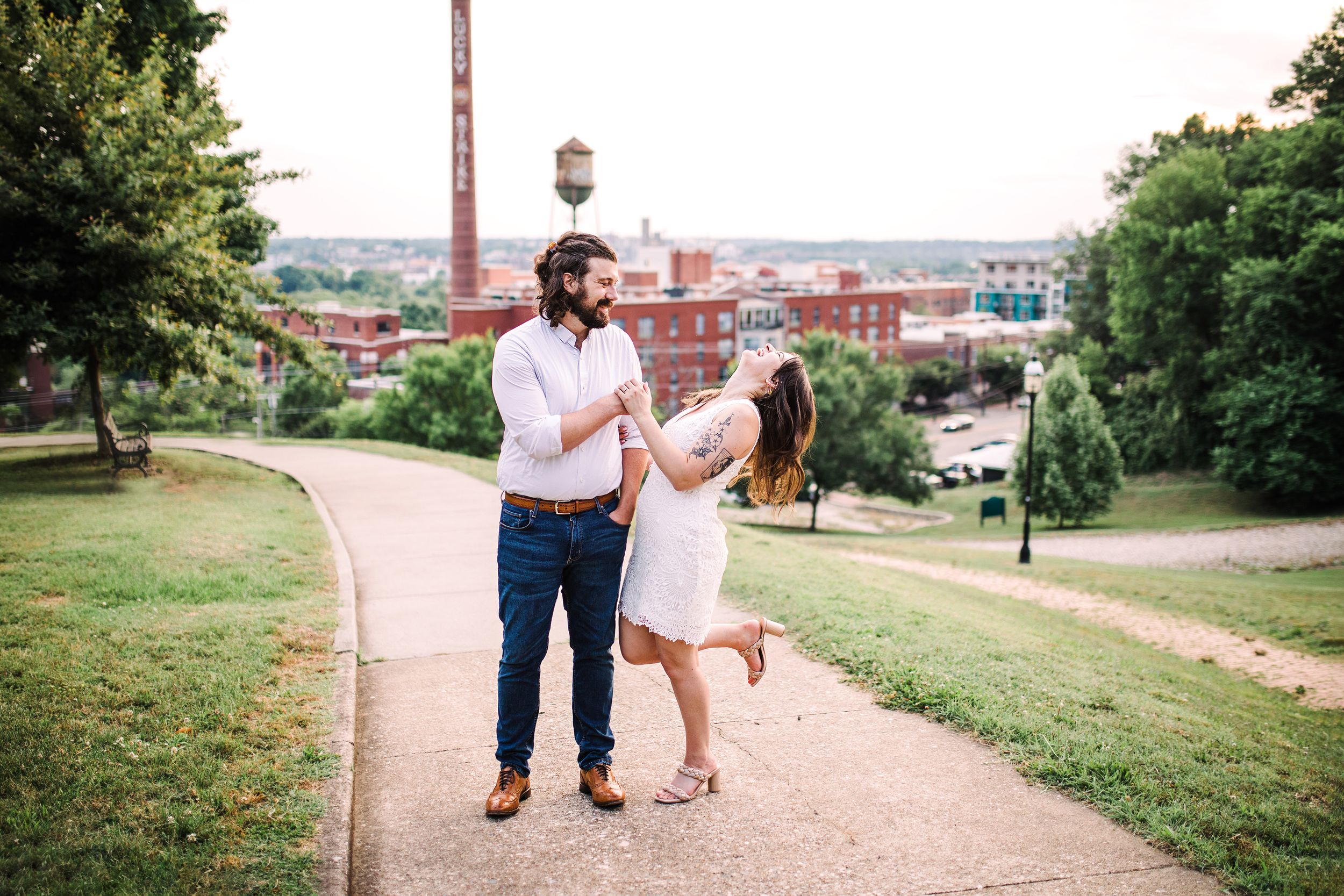 Happy couple dancing together on a scenic park path with urban skyline in background.