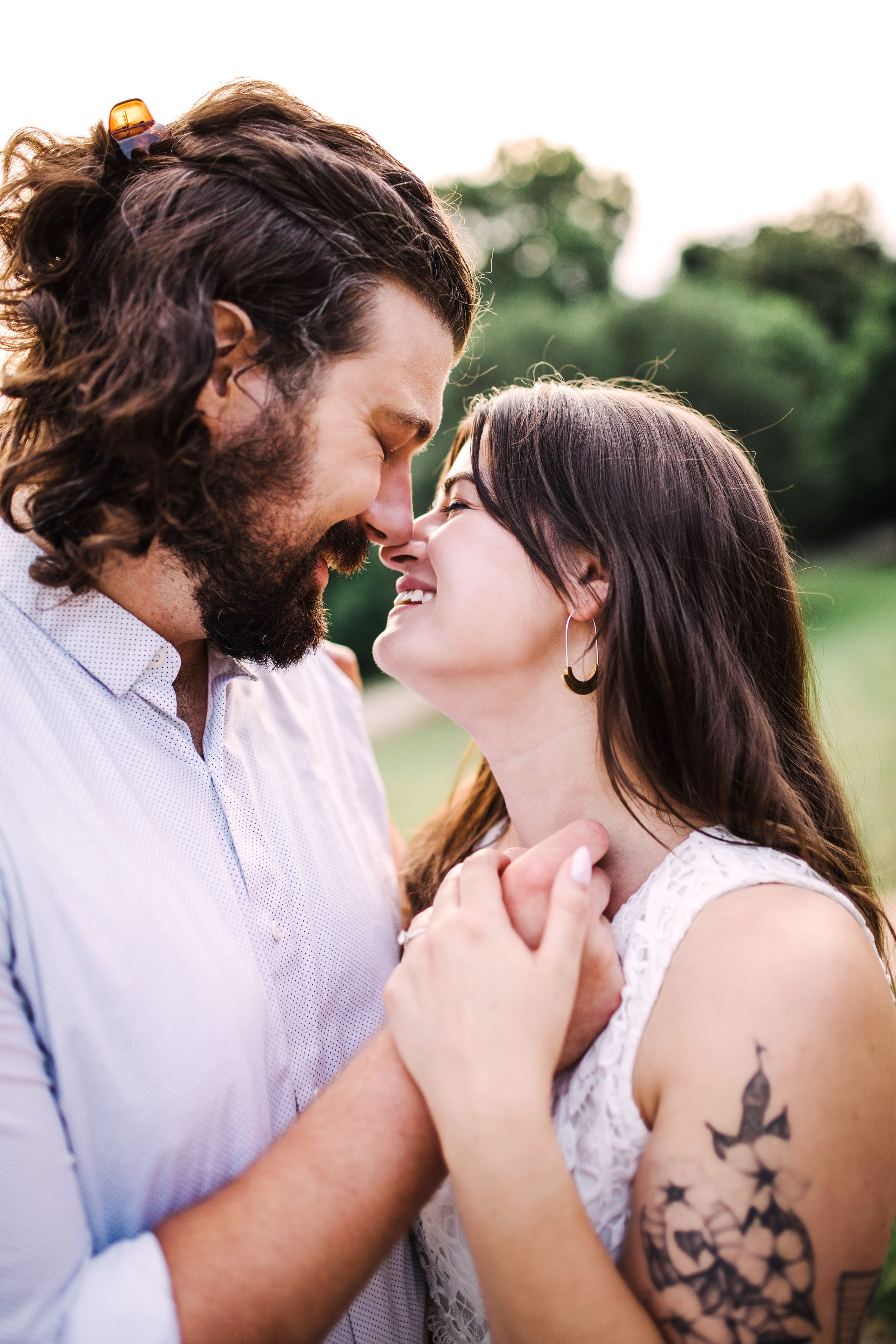 Couple sharing an intimate moment touching foreheads and smiling outdoors in a green park setting.