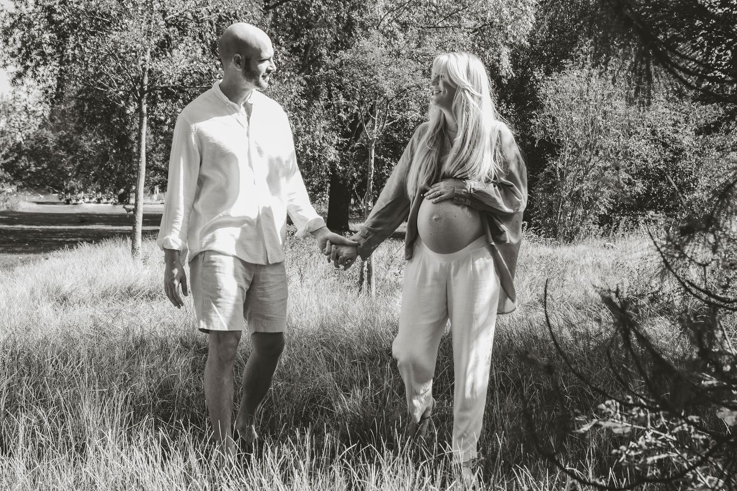 Black and white outdoor maternity photo of couple holding hands in nature, in Clissold park, Stoke Newington, London.