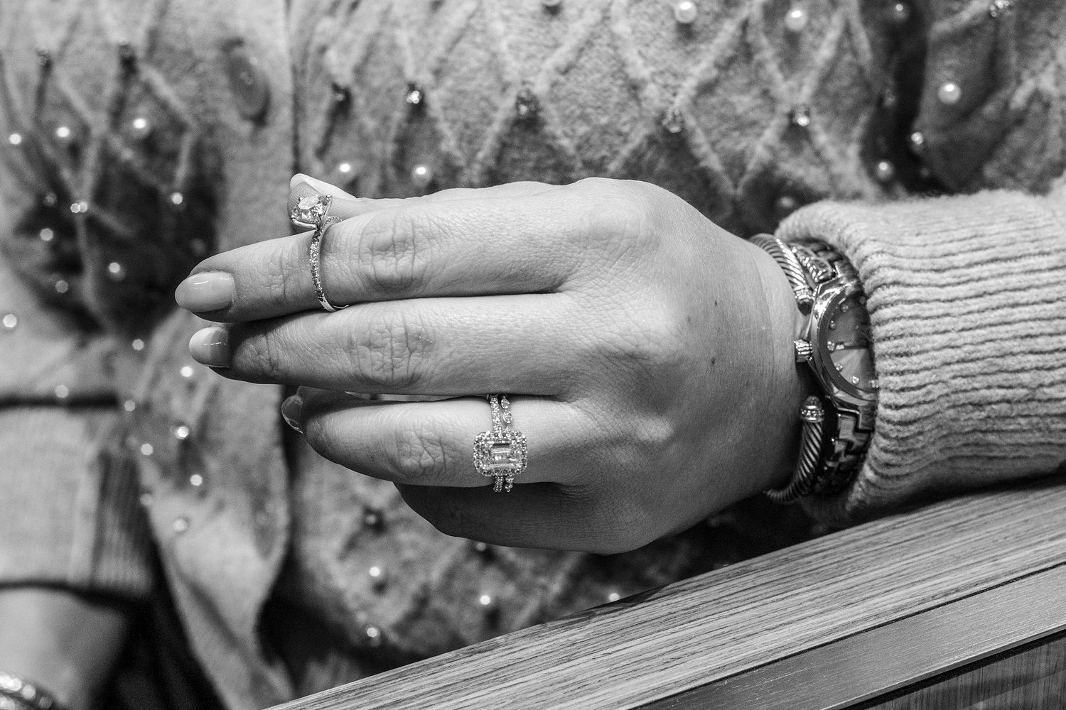Close-up of hand wearing multiple rings against textured fabric background.
