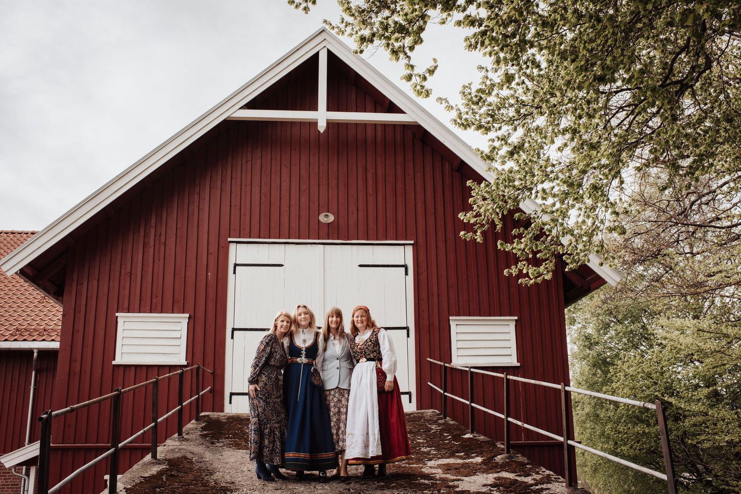 People in traditional Norwegian dress standing at entrance of a red wooden barn building.