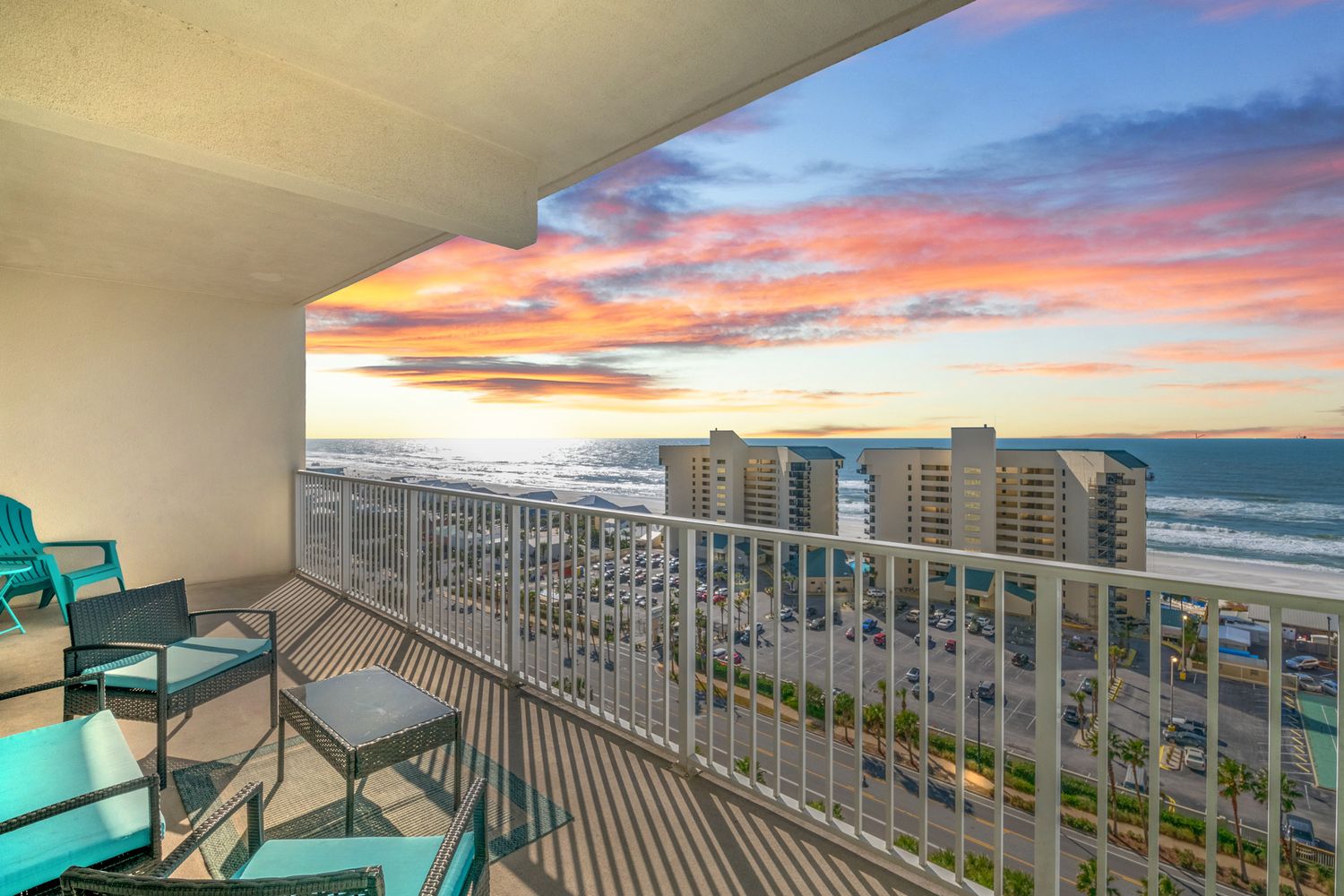 Beachfront balcony view at sunset with vibrant orange and pink clouds over coastal skyline.