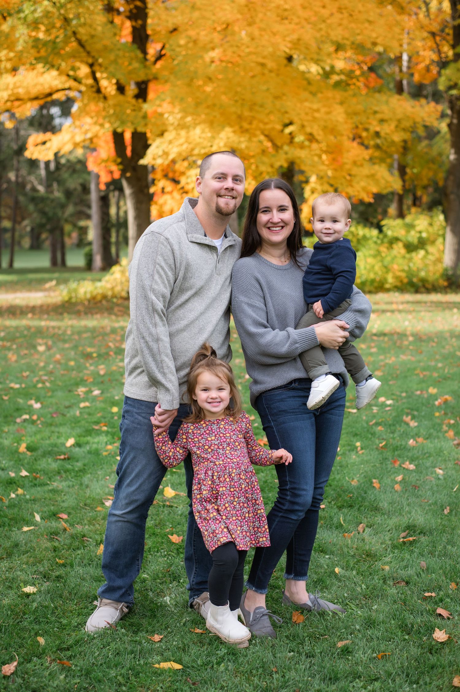 A family poses together on grass with vibrant fall foliage in the background.