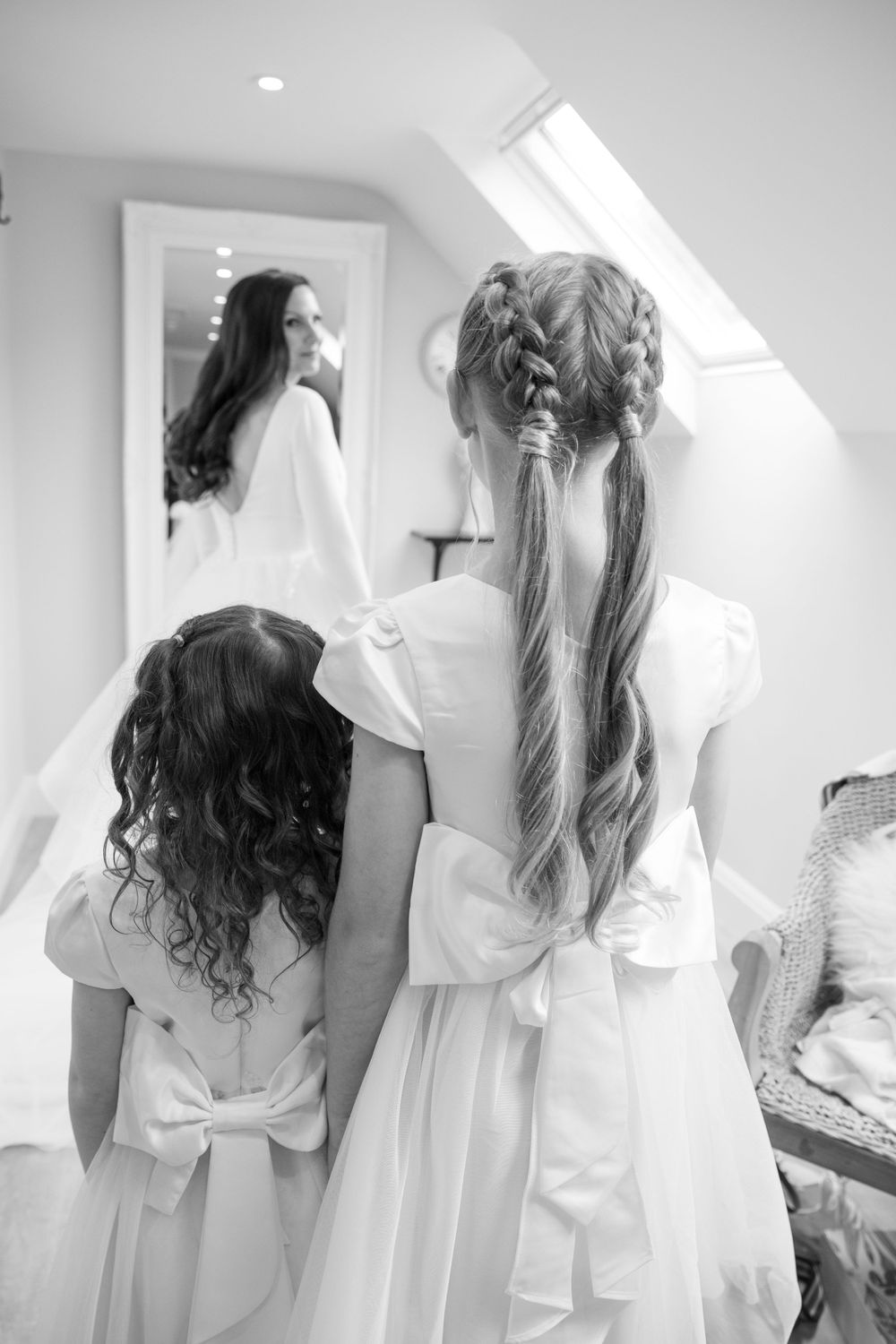 Black and white photo of young attendants in white dresses looking at a wedding gown.