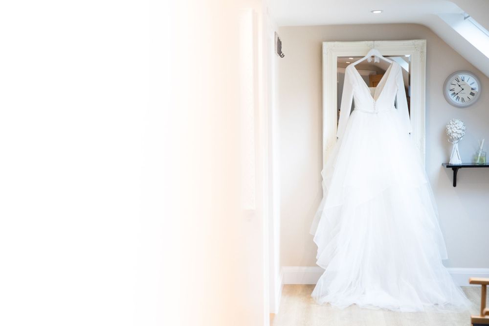 Elegant white wedding dress hanging in bright, minimalist room.