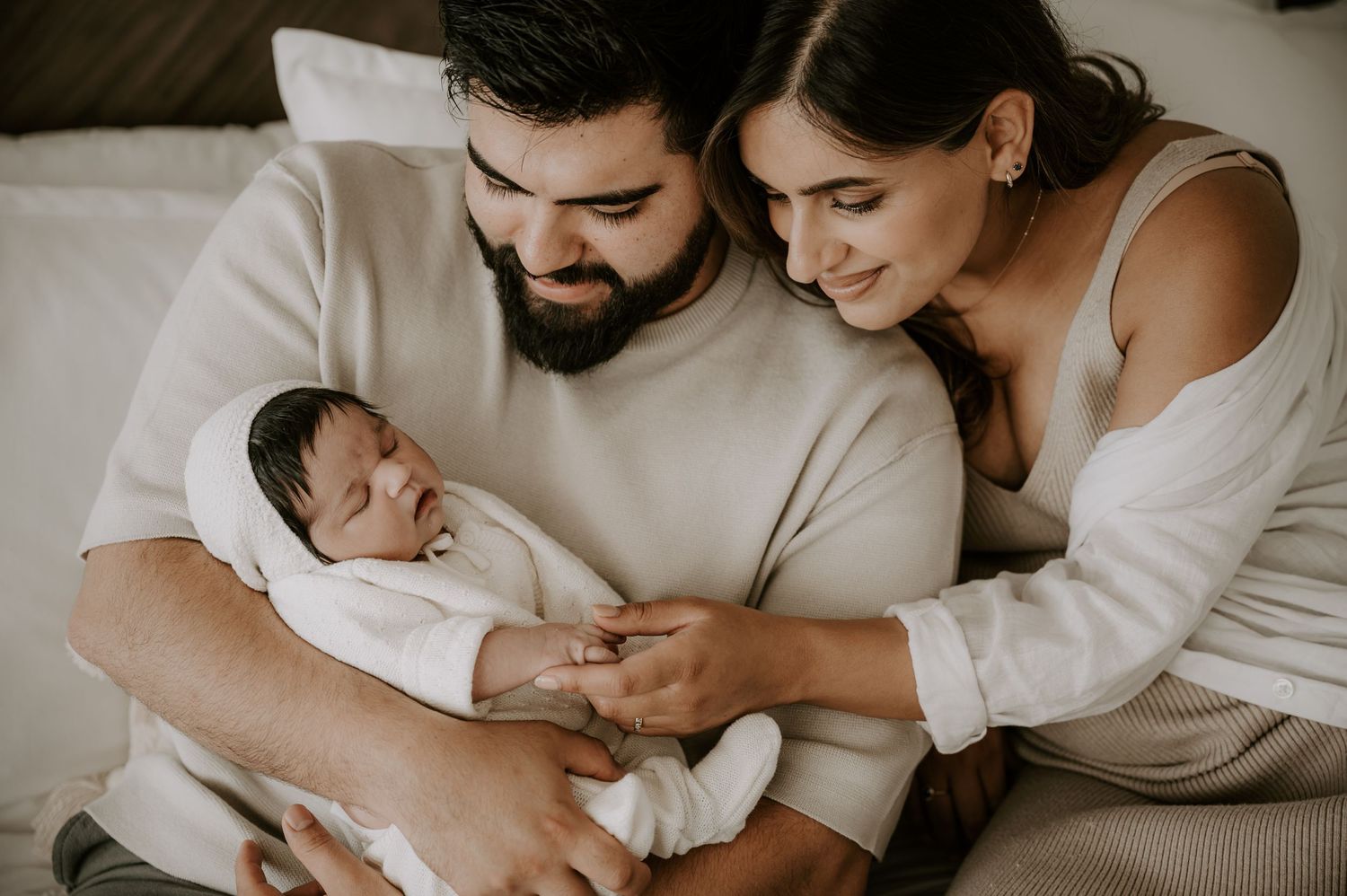 Tender moment with newborn baby wrapped in white against soft neutral background.