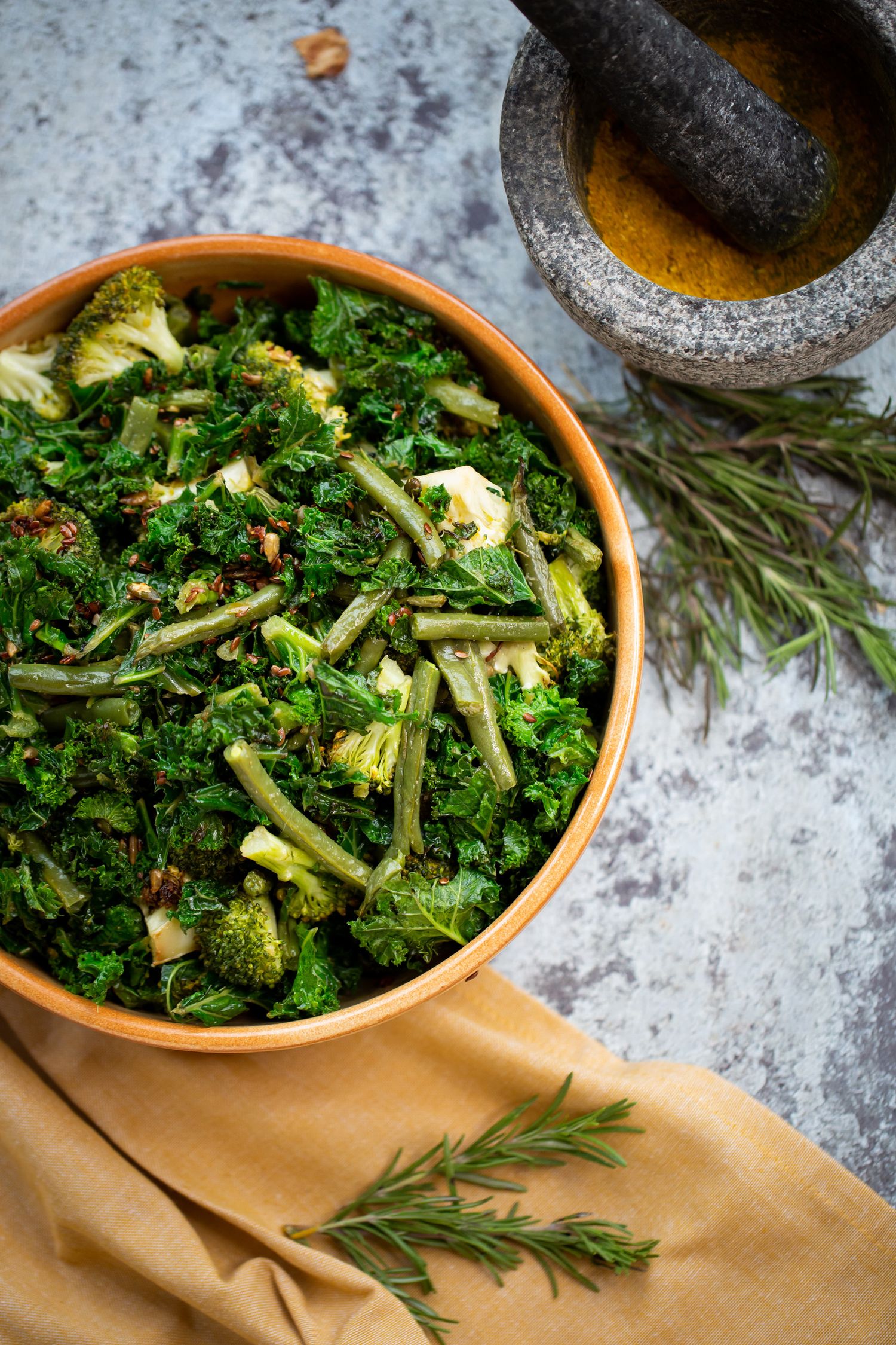 Fresh green kale and broccoli salad in terracotta bowl with herbs and mortar pestle.