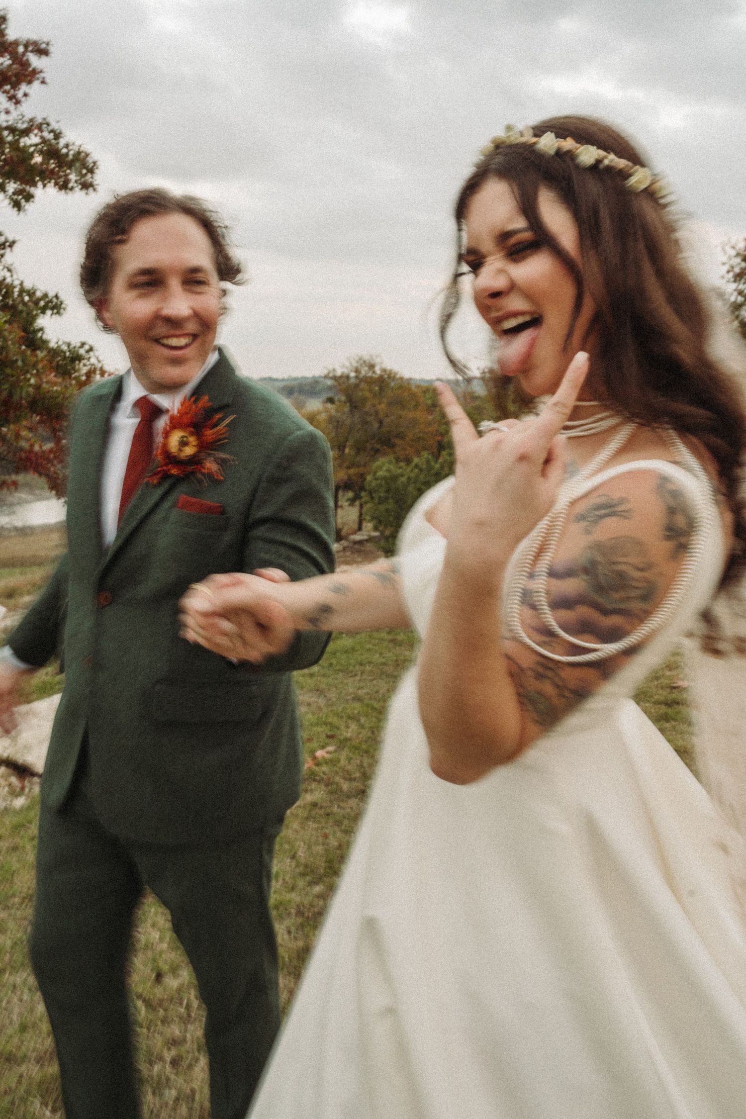 A joyful wedding moment captured outdoors with the couple laughing together, showing tattoos and floral details.