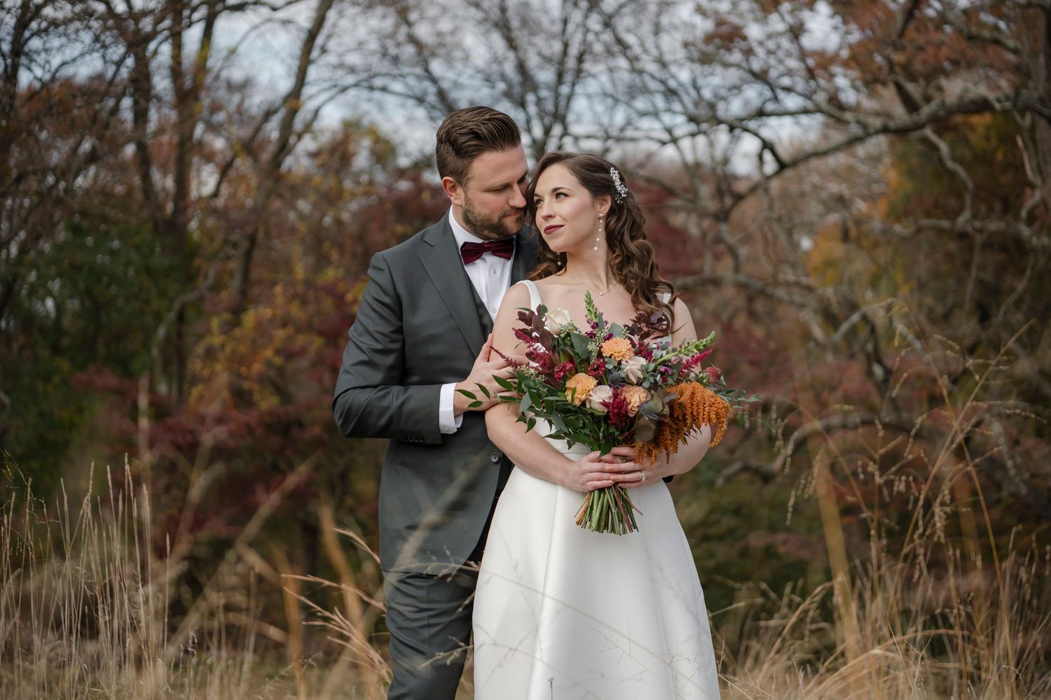 groom holding his bride from behind in an open field during autumn