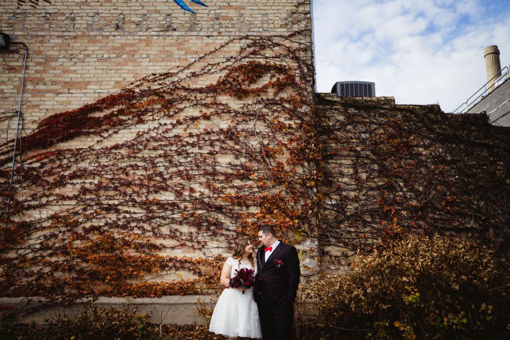 Wedding couple posing against rustic brick wall backdrop on their special day.