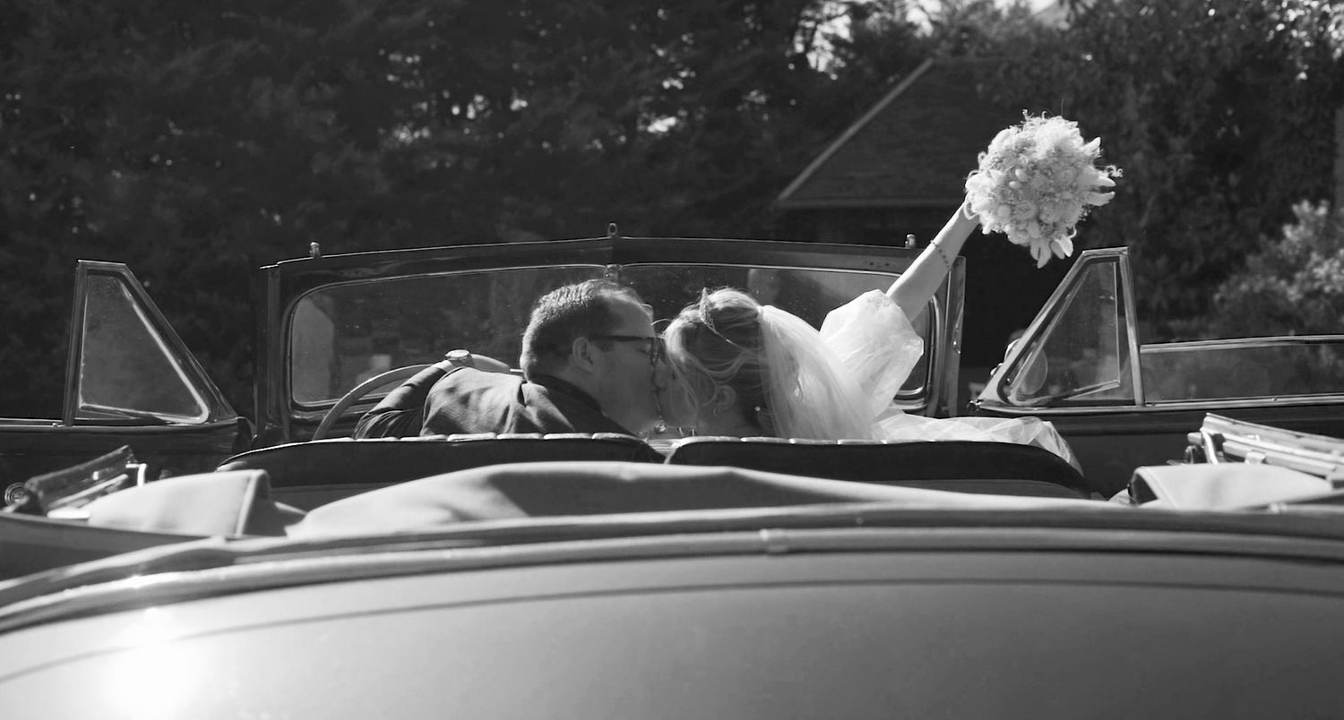Black and white panoramic view of a classic car at a wedding venue.