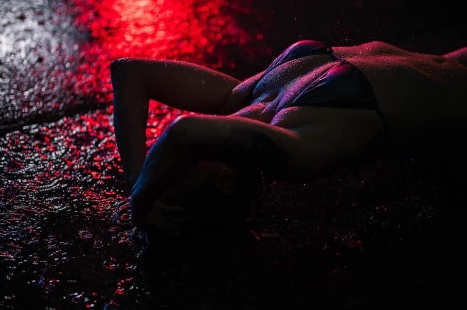 Silhouette of a figure lying down illuminated by dramatic red and blue lighting against a dark textured background.