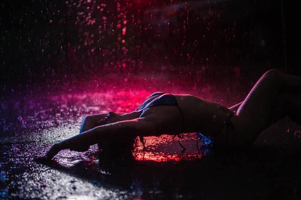 Artistic silhouette lying in water illuminated by dramatic pink and purple lighting effects.