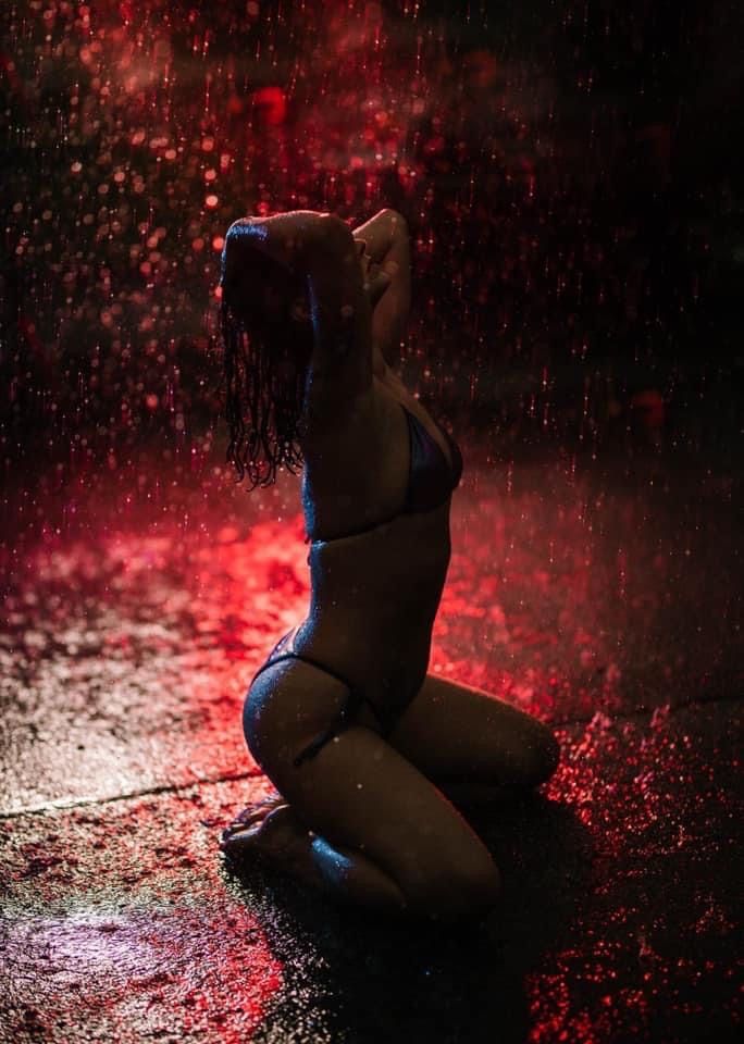 A silhouetted figure kneels in dramatic red lighting with water droplets creating a moody atmospheric effect.