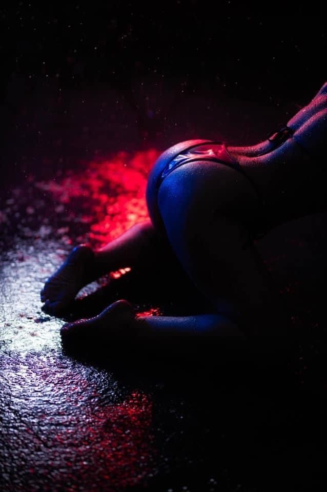 Atmospheric dark photo with person lying on wet ground illuminated by dramatic red and blue lighting effects.