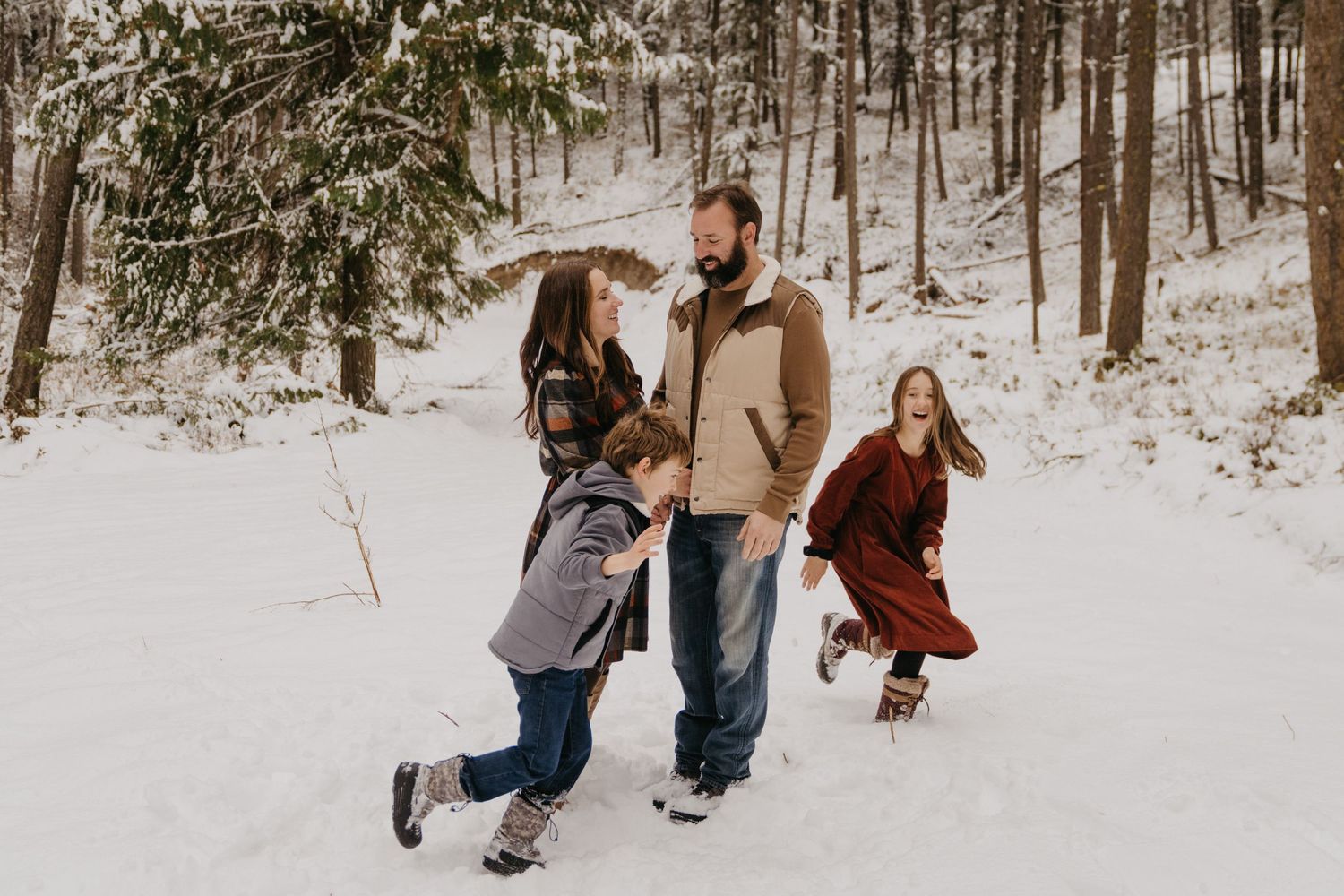 People playing and running through a snowy forest landscape together.