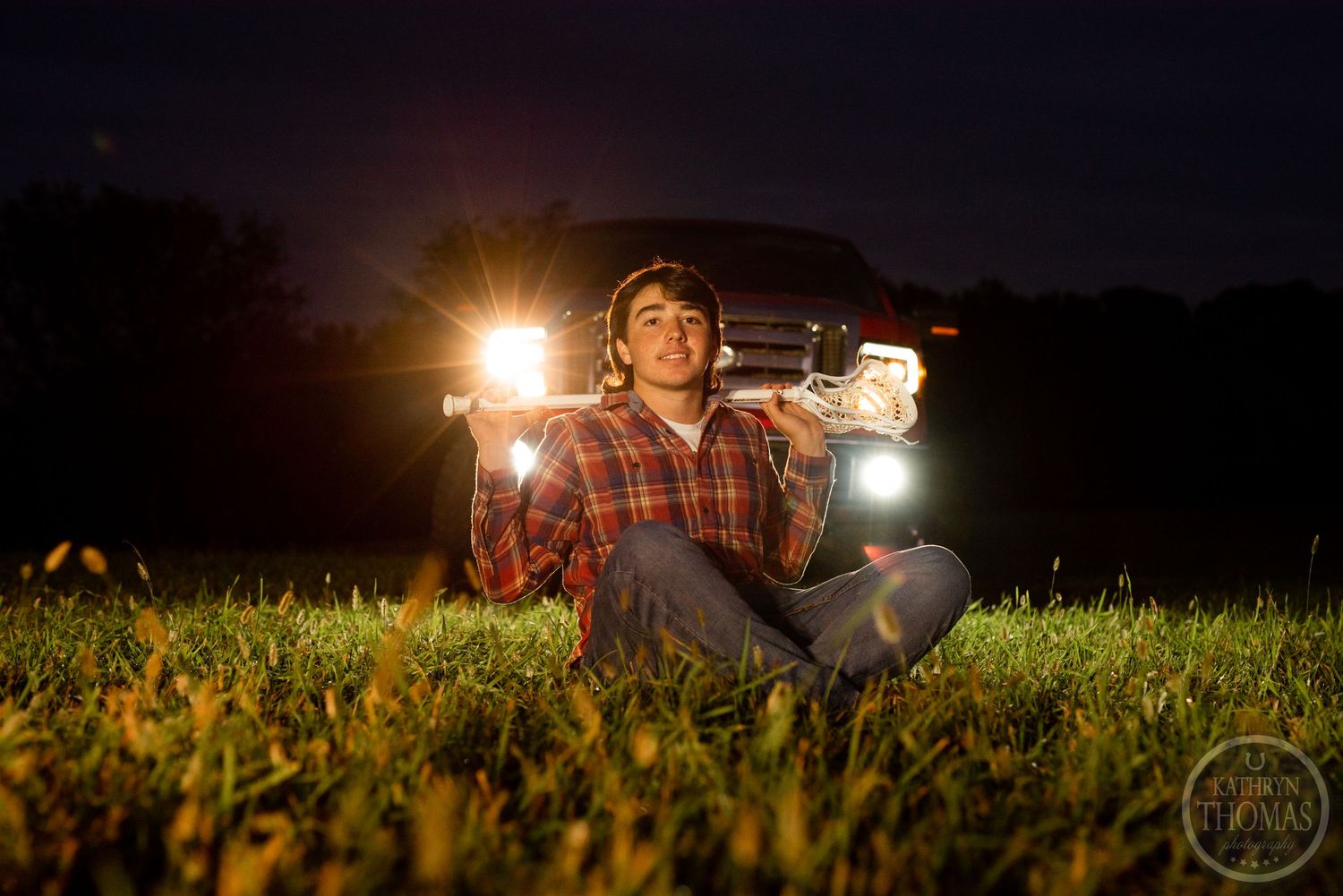 Person holds lanterns in a dark field with truck headlights glowing in the background at night.