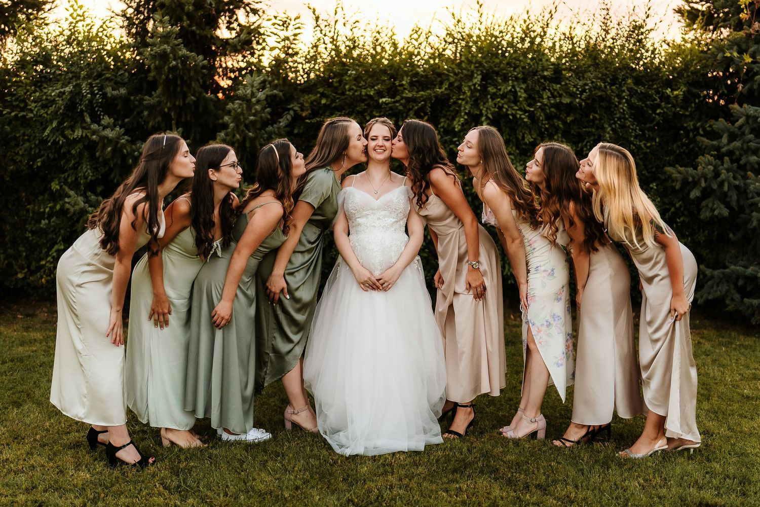 Wedding party forming circle around bride in outdoor garden setting at sunset.