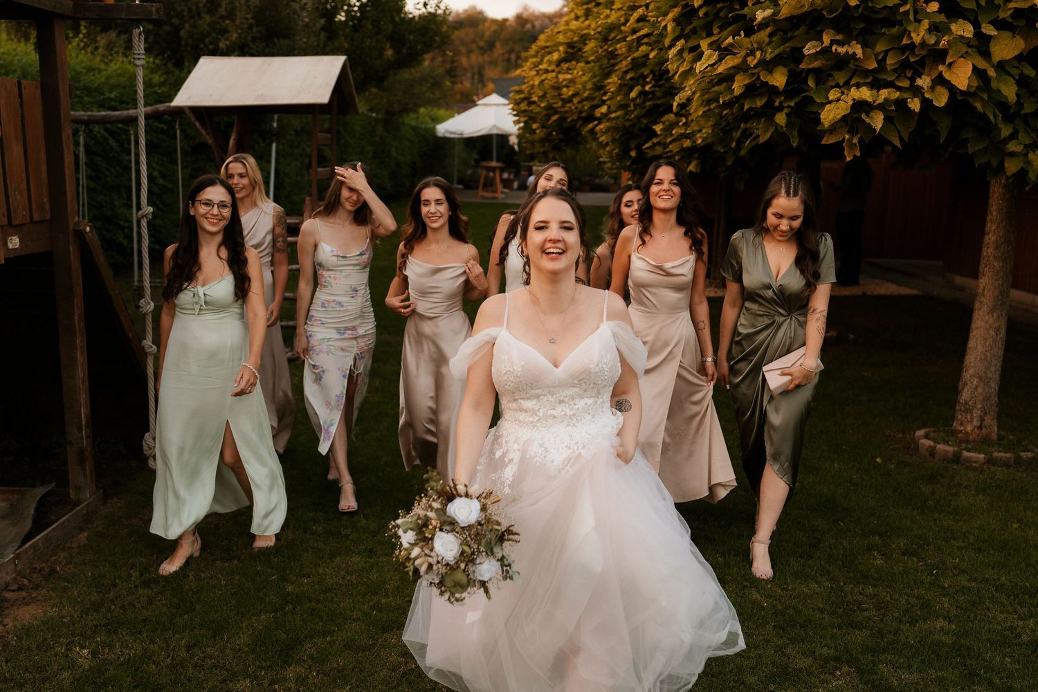 Bridal party following bride through garden setting in evening light.