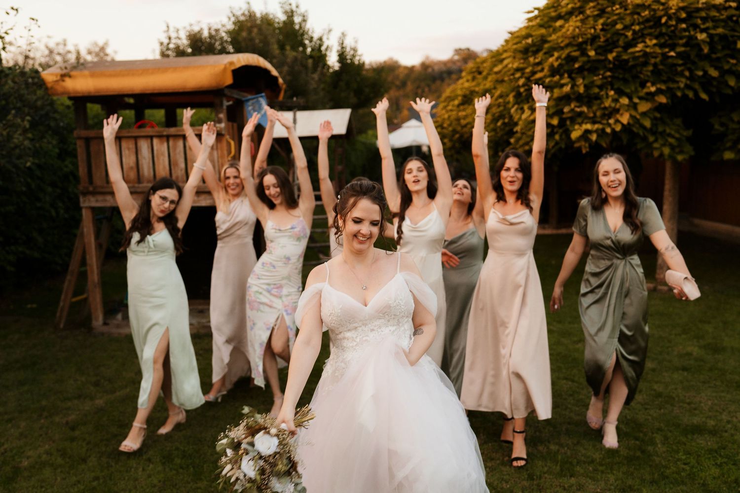 Bridal party jumping and celebrating behind bride in backyard garden setting.
