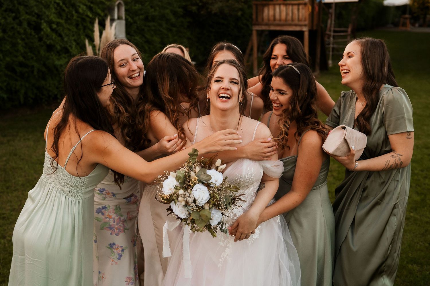 Wedding party sharing candid laughter with bride holding white bouquet.