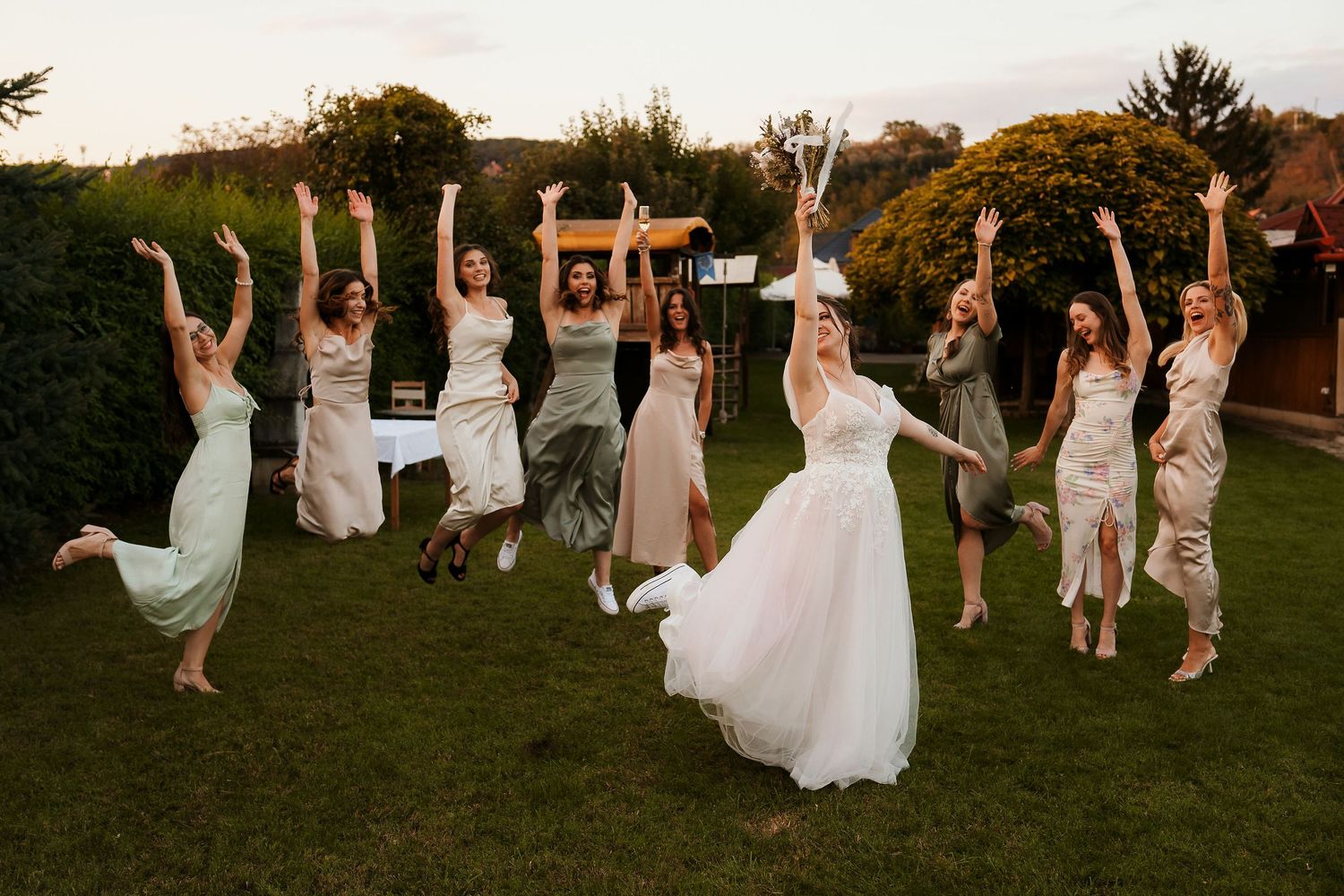 Wedding party jumping in celebration on lawn with bride in center.