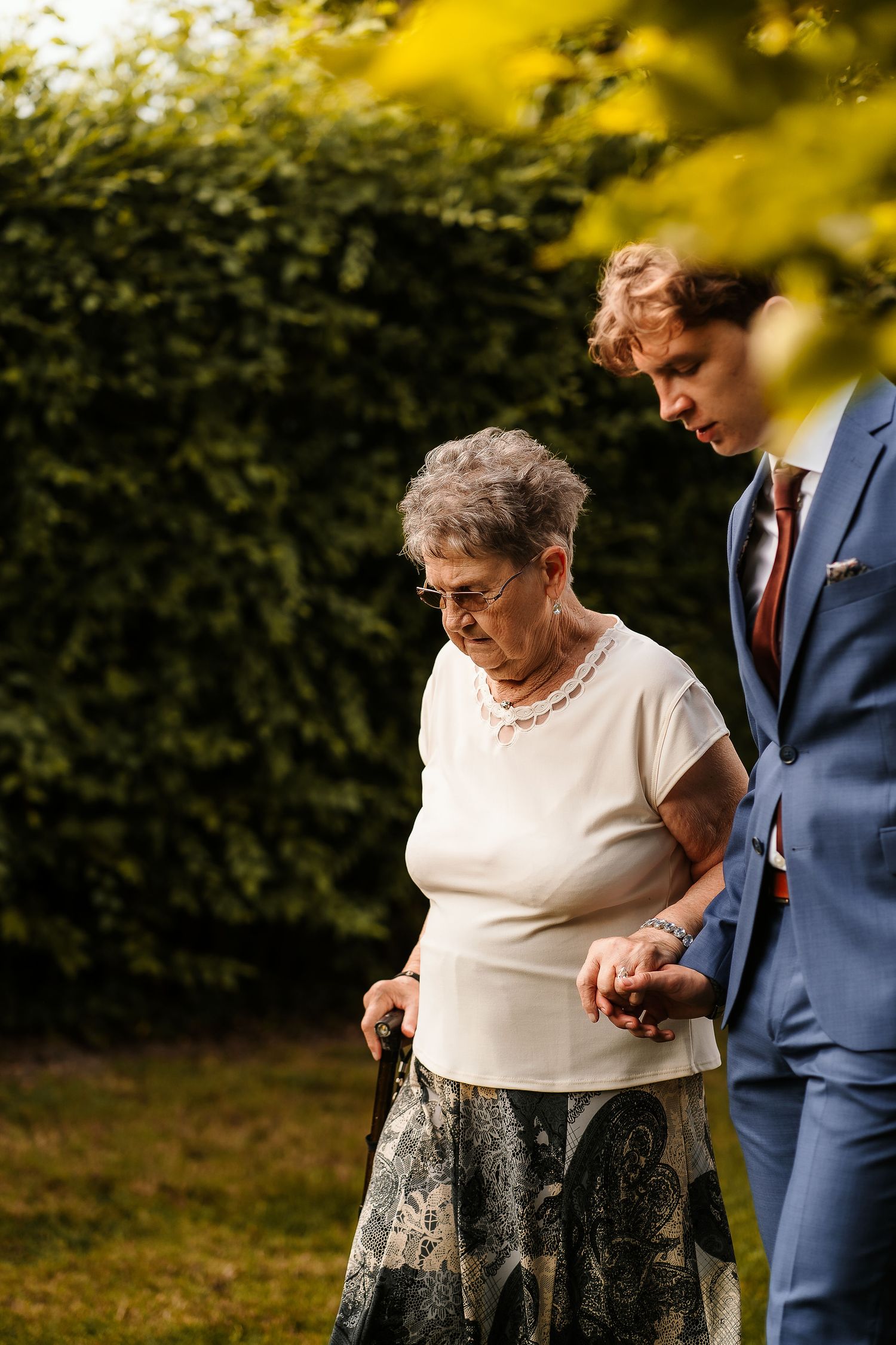 A tender outdoor moment between two people during a wedding event near a garden hedge.