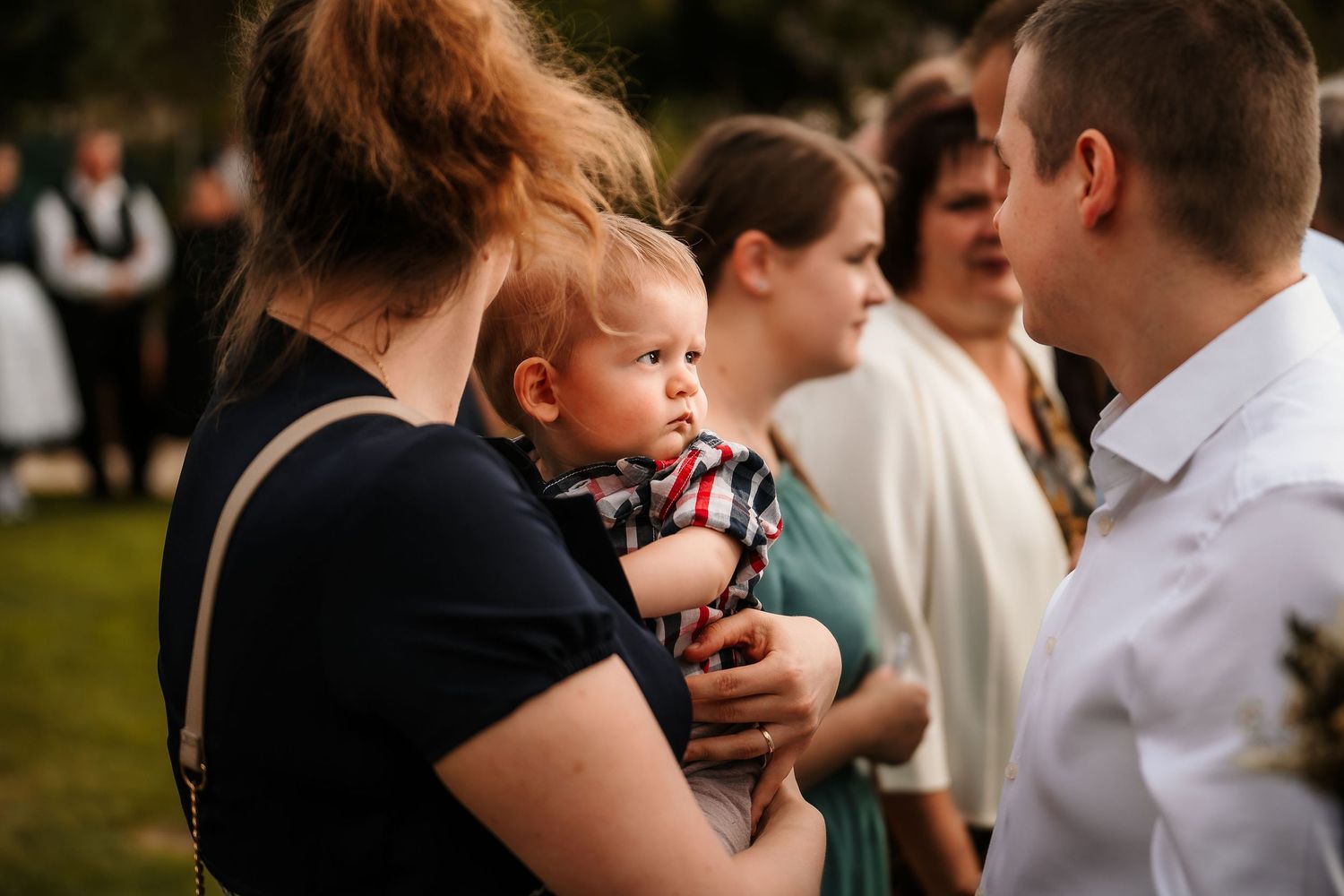 A small child being held during an outdoor wedding reception gathering.