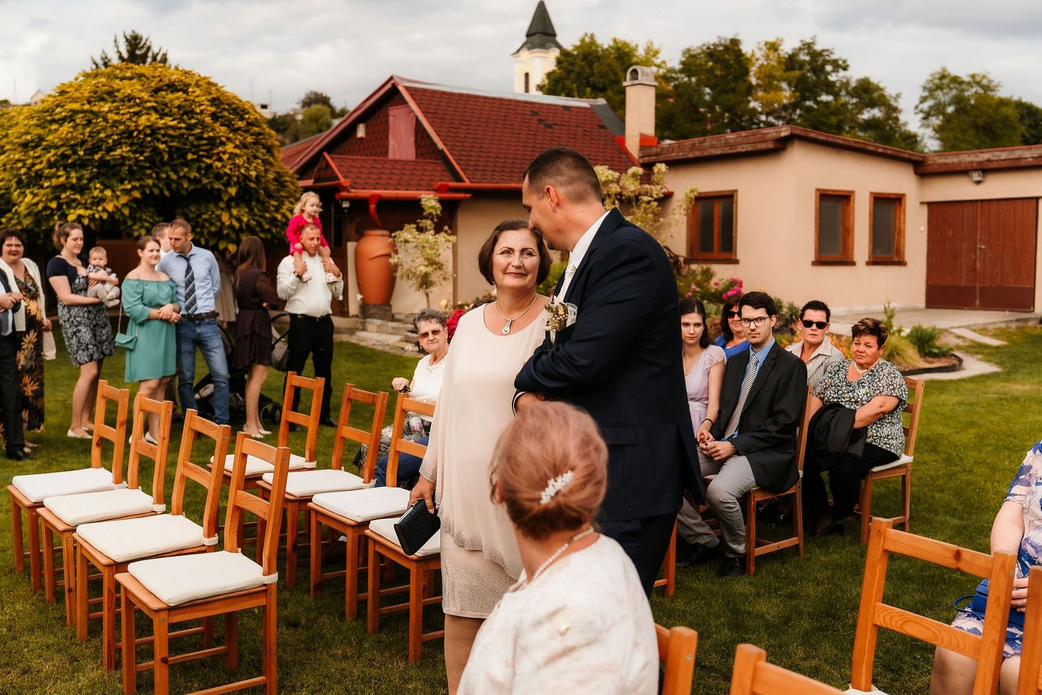 Outdoor wedding ceremony setup with wooden chairs on a lawn in front of a rustic building.