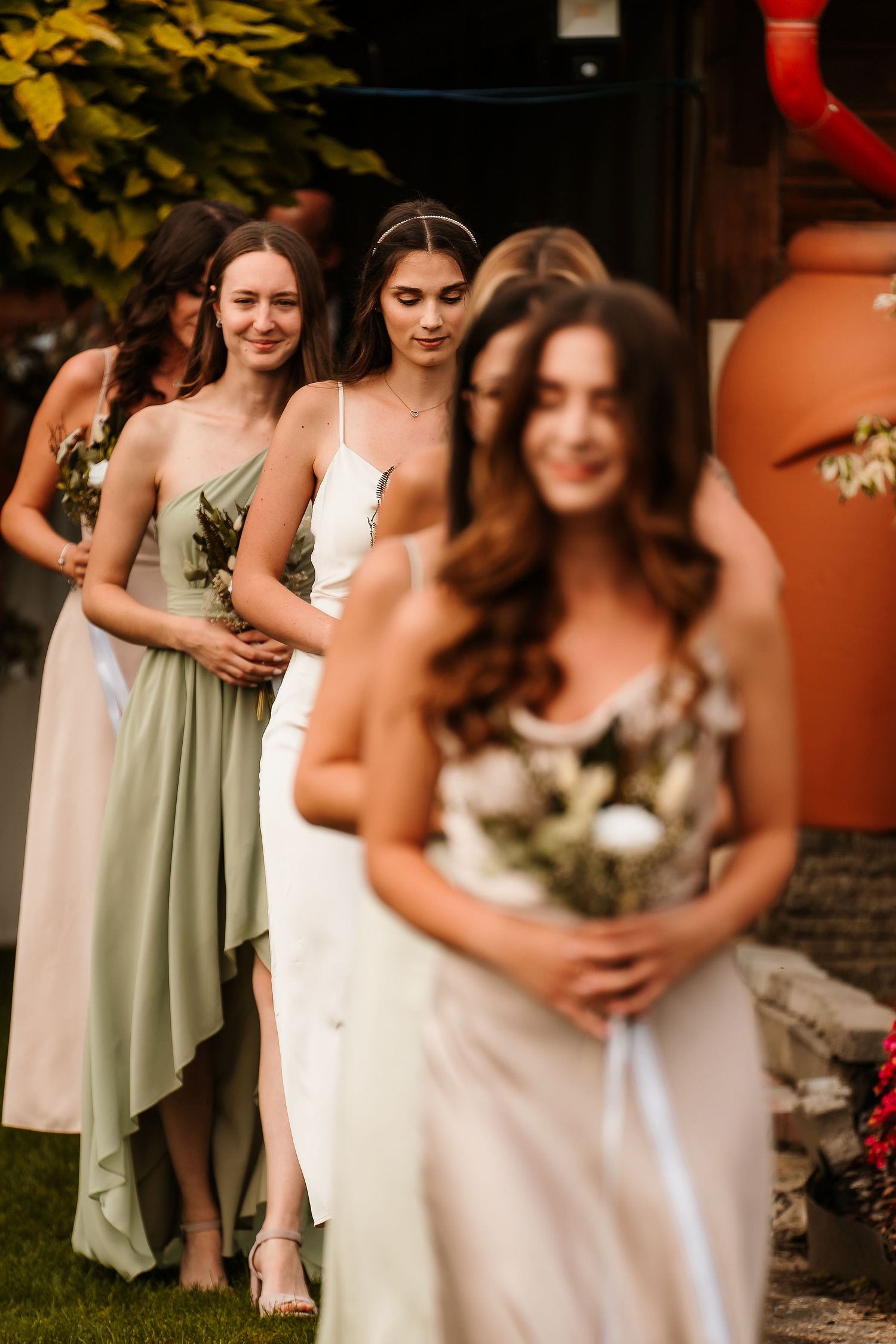 Line of bridesmaids in pastel dresses holding bouquets during an outdoor wedding ceremony.