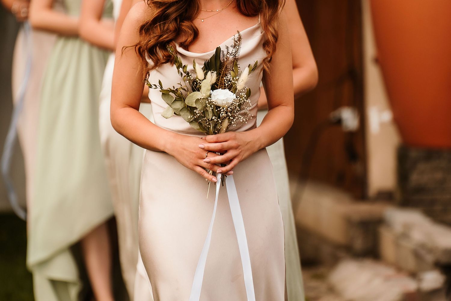 Close-up of bridesmaid holding a white and green bouquet against a light silk dress.