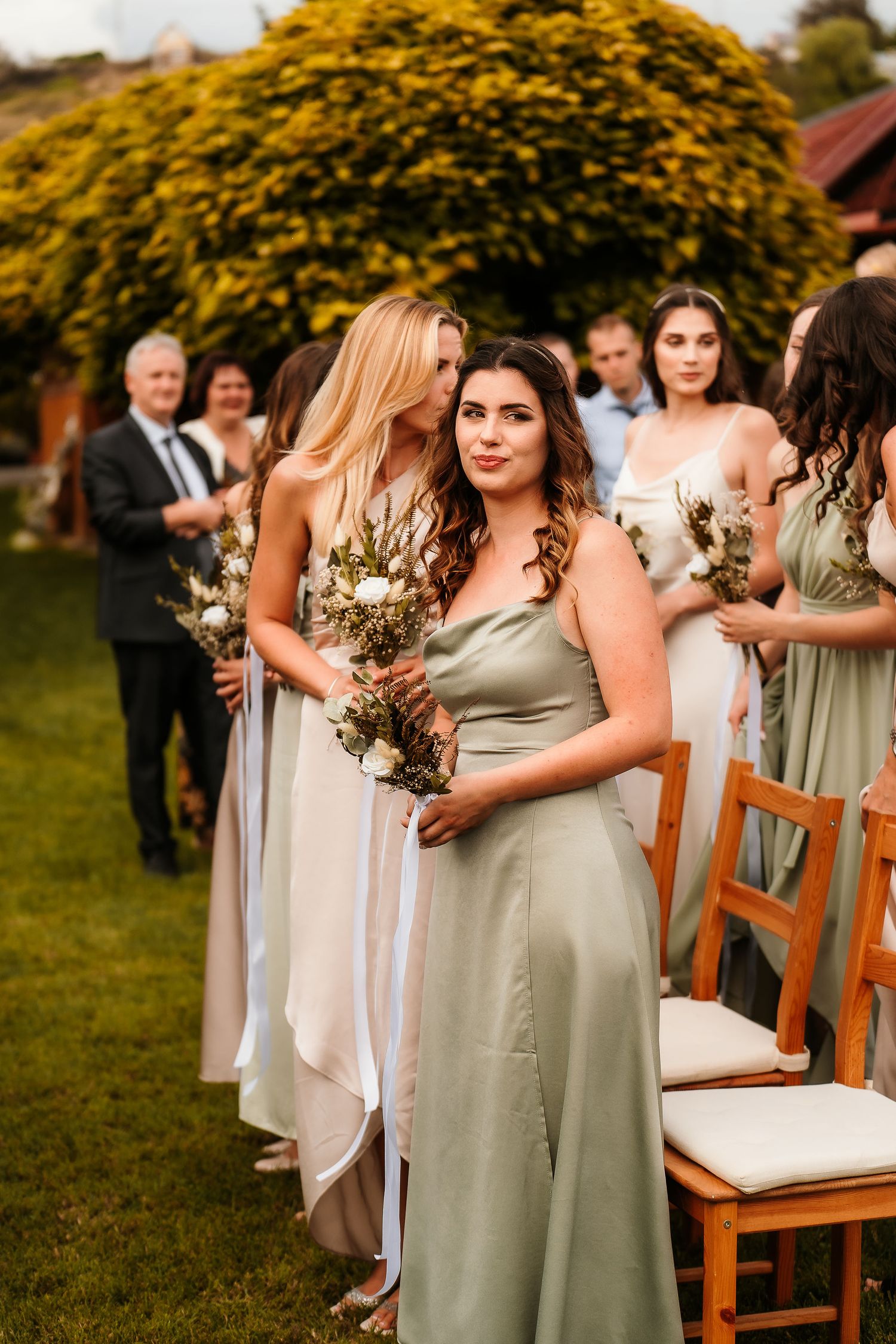 Bridal party in mix-and-match pastel dresses standing in a garden setting.