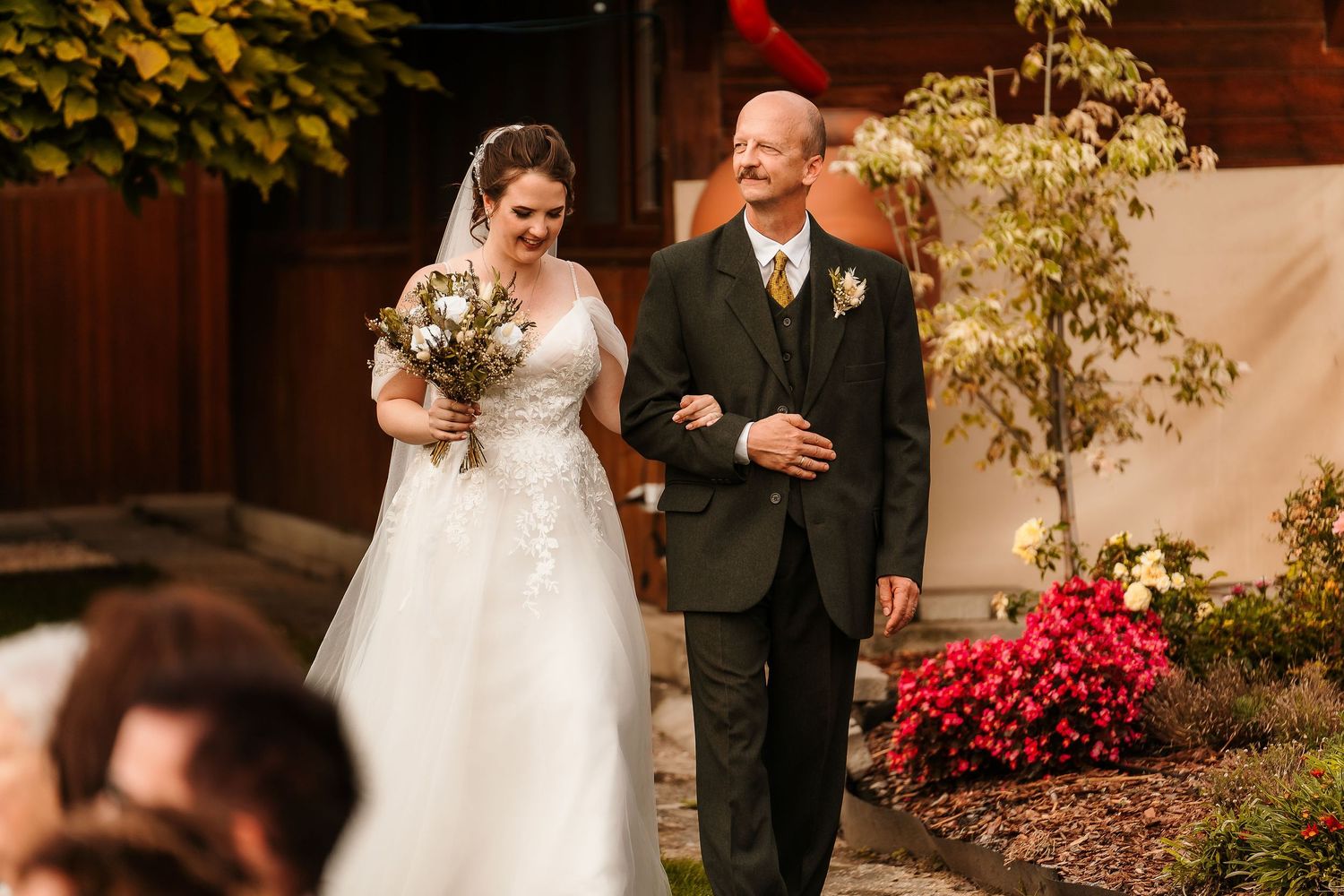 Wedding processional on stone path with red flowers and autumn foliage in background.