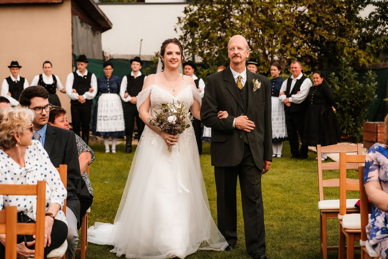 Wedding ceremony in garden setting with traditional decor and wooden chairs.